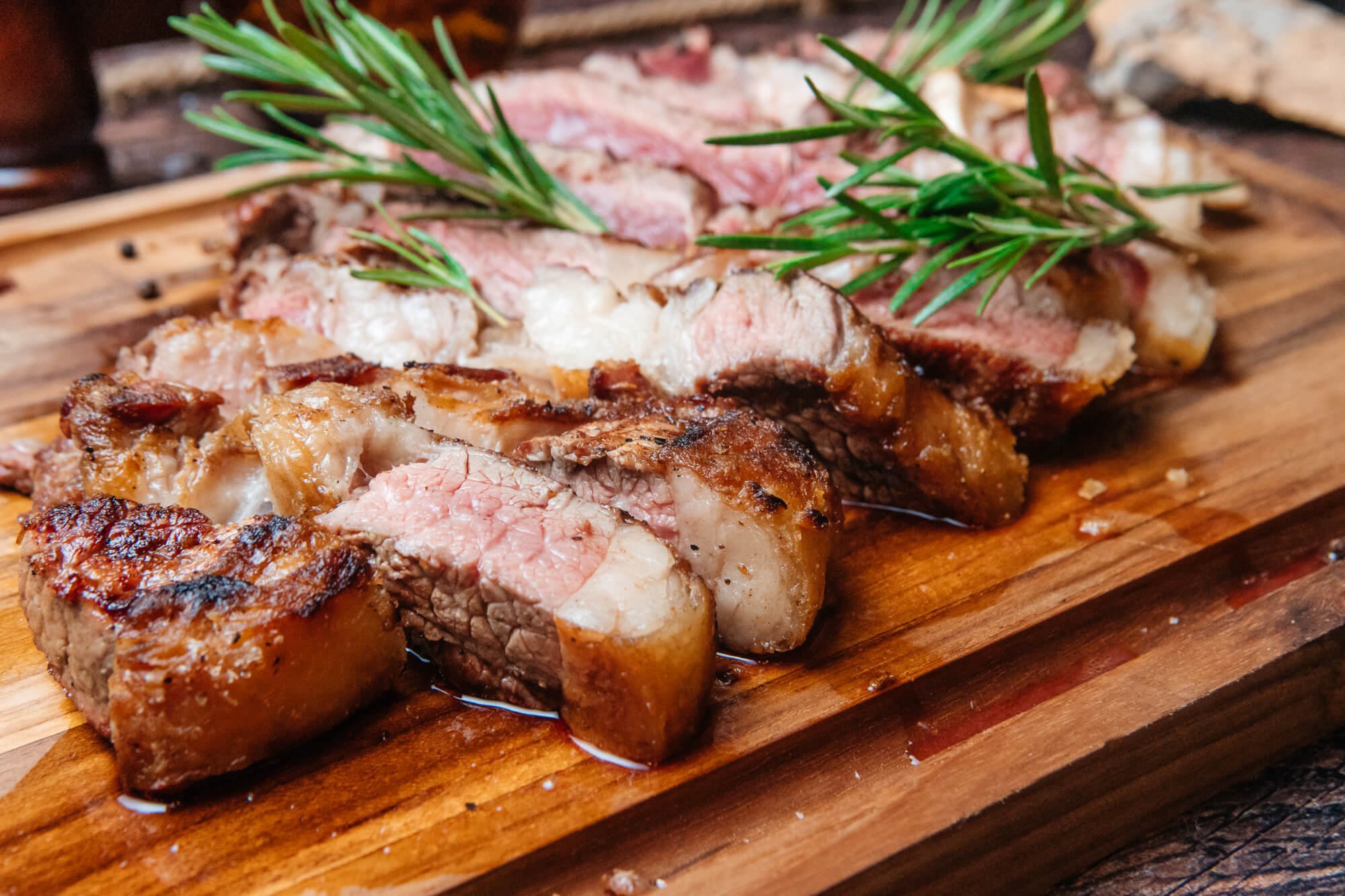Carne asada en rodajas con romero sobre una tabla de madera.