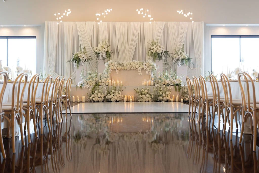 Elegant wedding reception setup with white drapes, floral arrangements, candles, and a dance floor