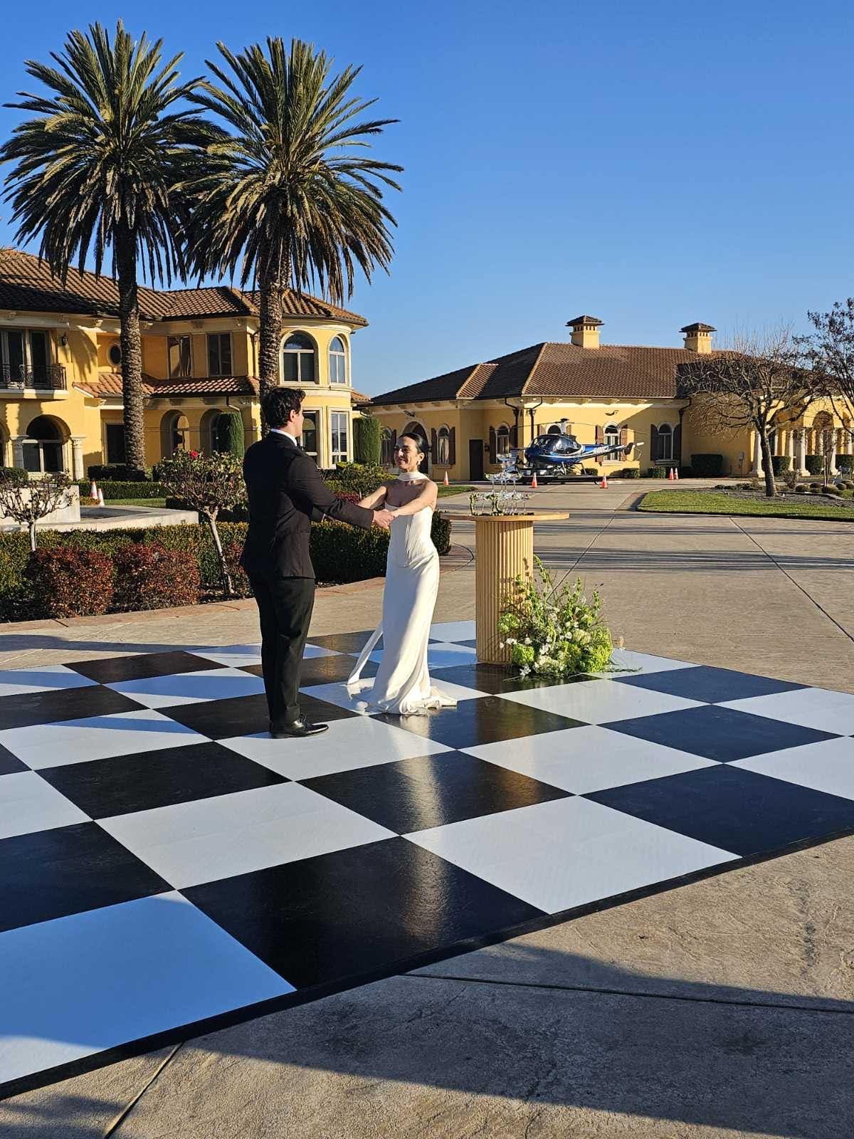 A couple is dancing on a large outdoor black and white checkered dance floor.