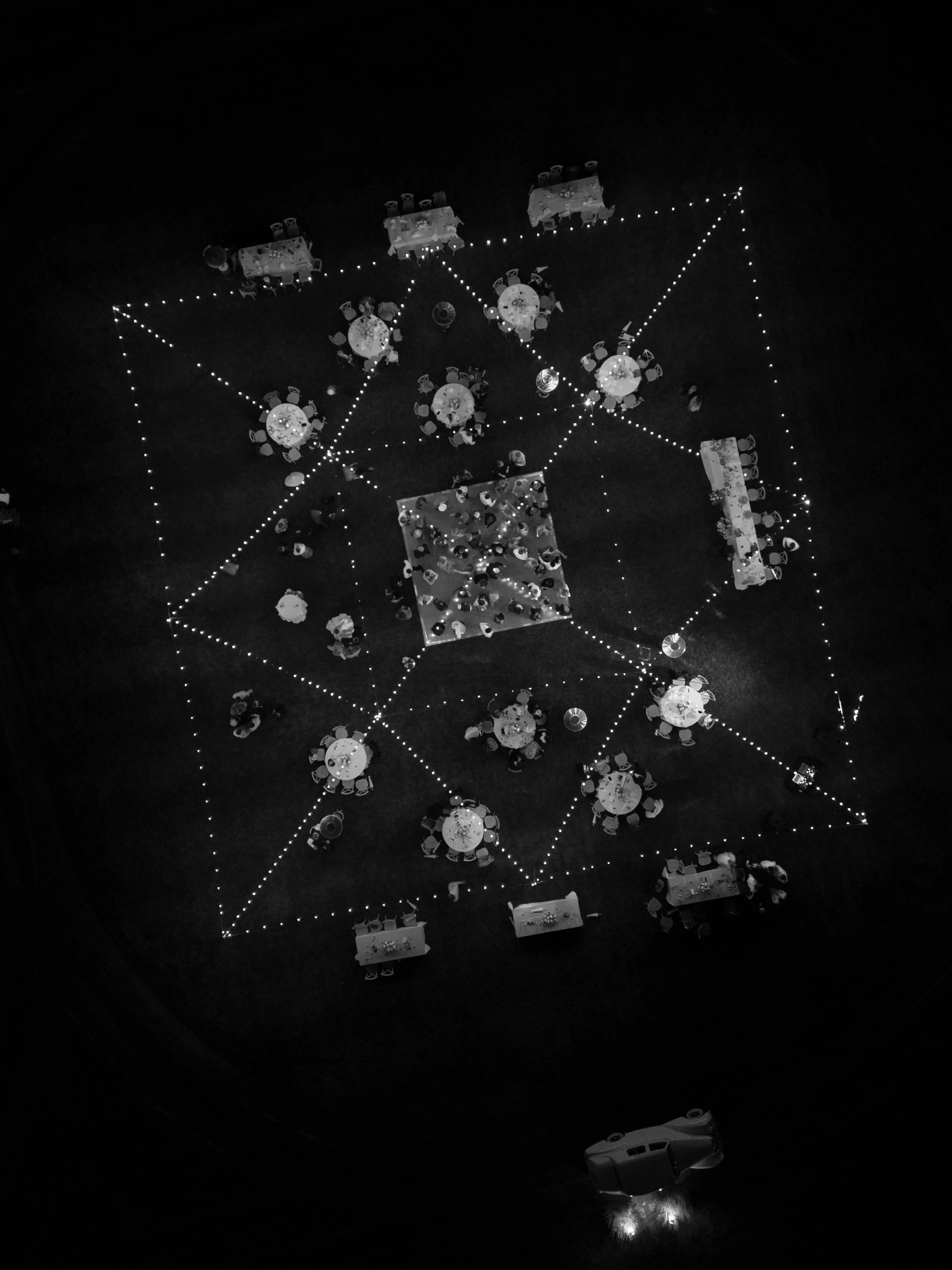 Overhead view of a large outdoor event at night with decorated tables, string lights, and a dance floor, seen from above.