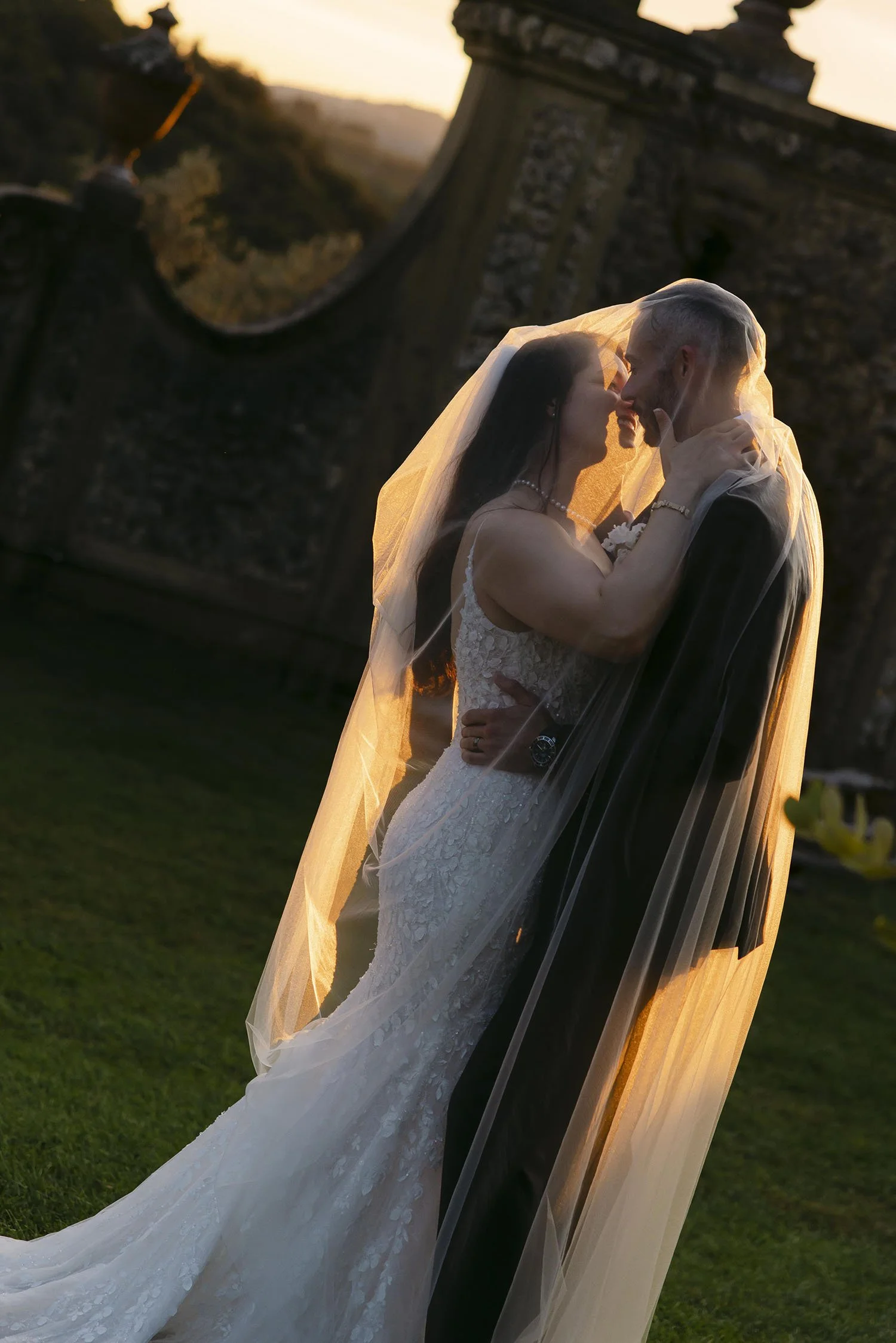 Bride and groom kissing under the veil with a dramatic sunset light