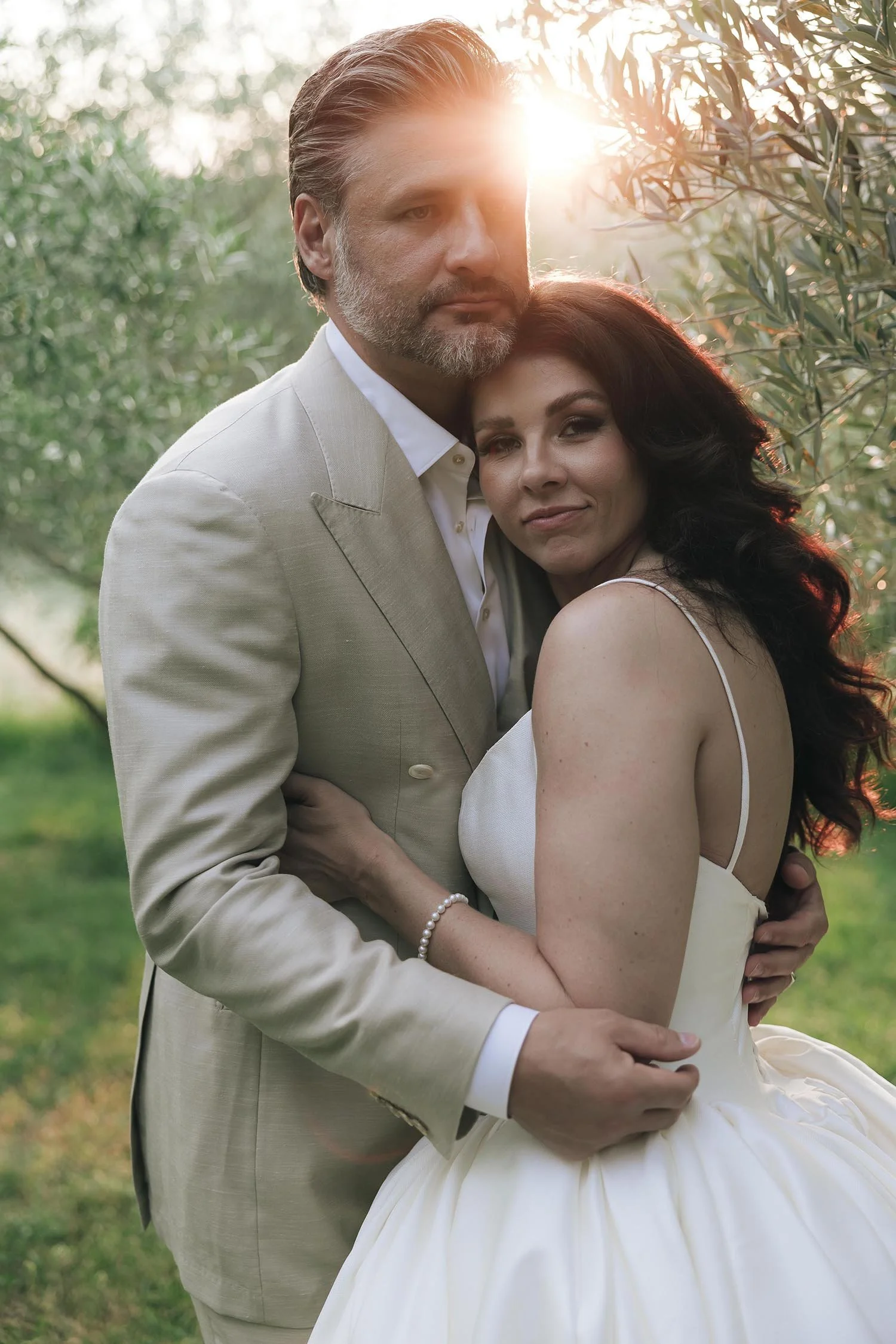 portrait of the groom holding the bride through the olive trees with the sun setting