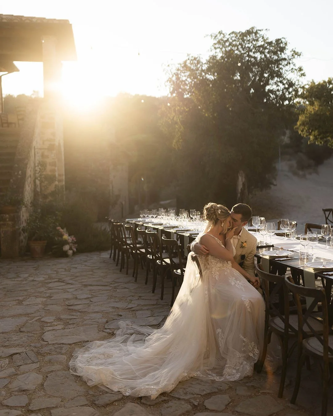 romantic moment of bride and groom sitting together at the dinner tables and kissing under the sunset