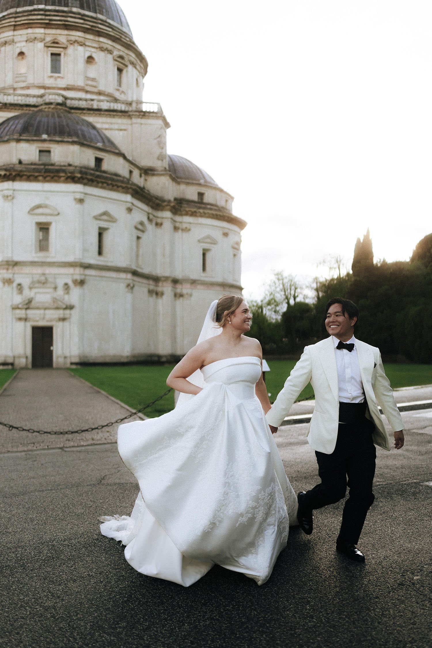 bride and groom running and crossing the road with a beautiful church in the background in Todi, Umbria
