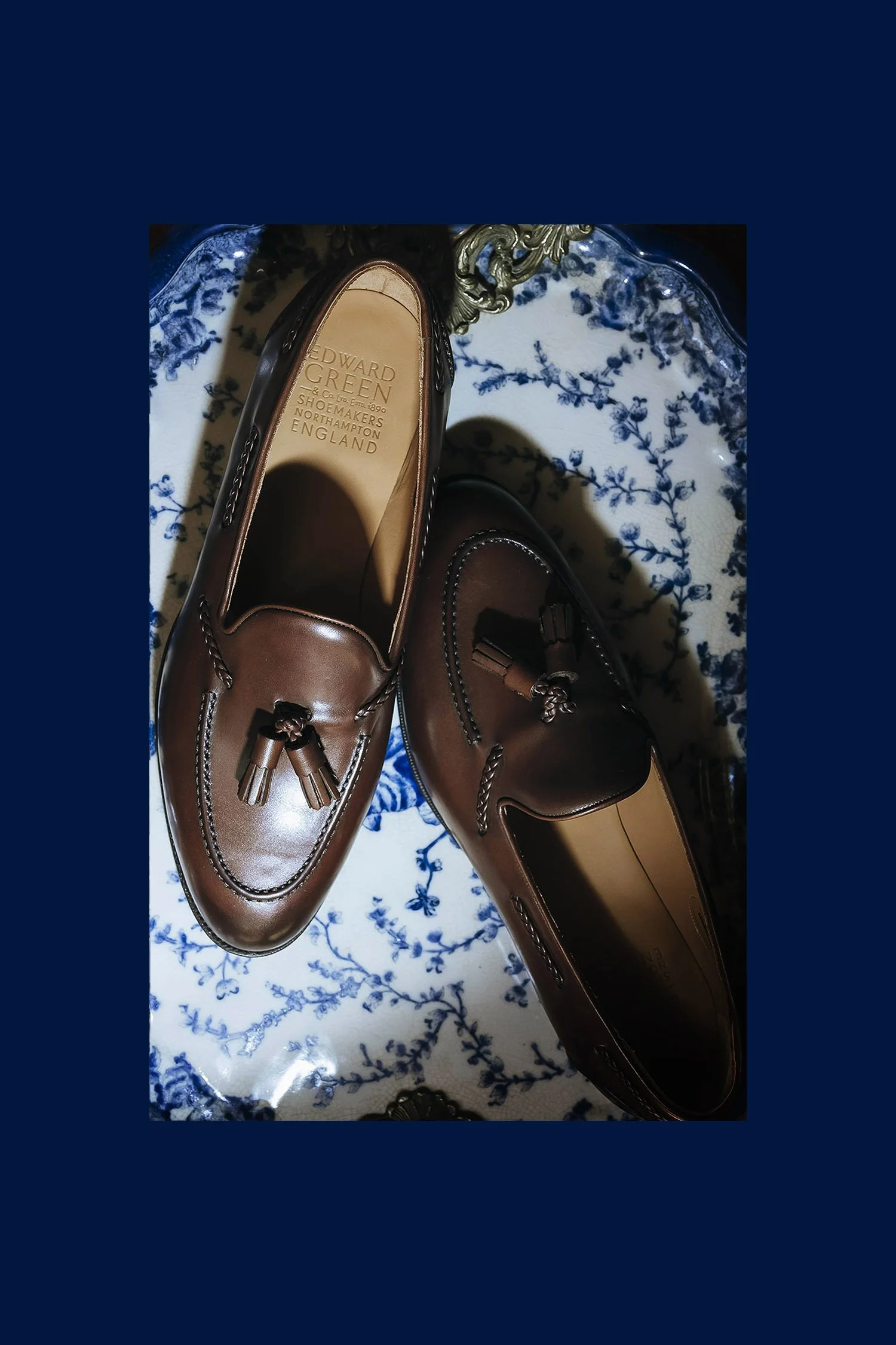 Pair of brown leather tassel loafers on a blue and white floral patterned tablecloth.