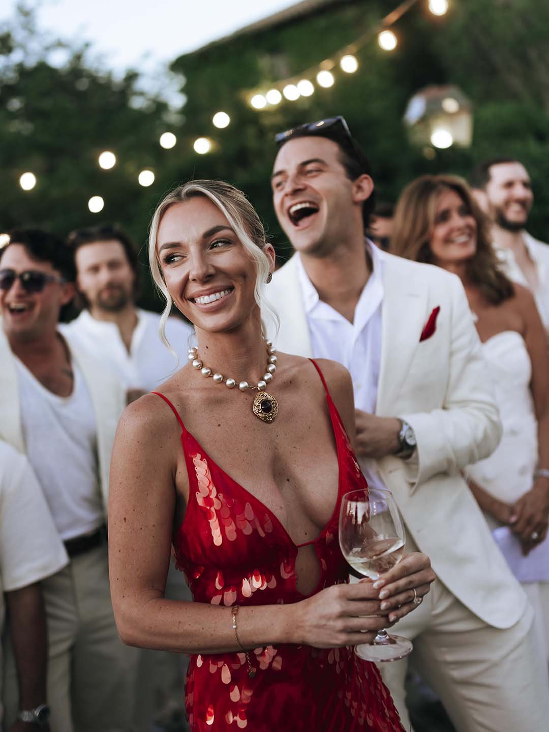 the bride wearing red and the groom wearing white laughing together with their guests