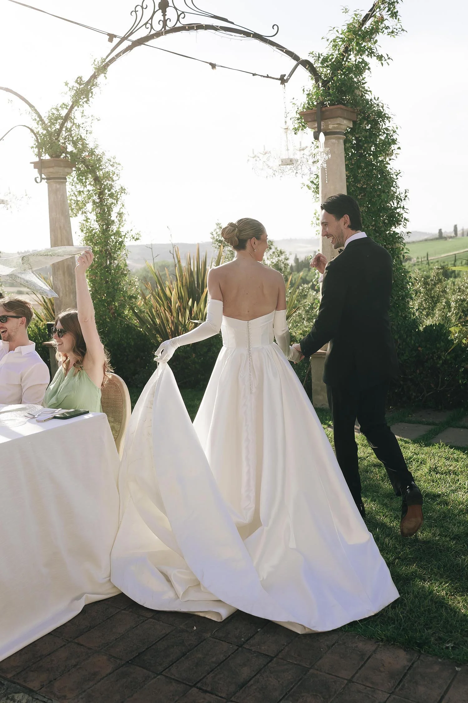 bride and groom walking togeter to the tables with the guests celebrating waving napkins in the air at Tenuta Corbinaia