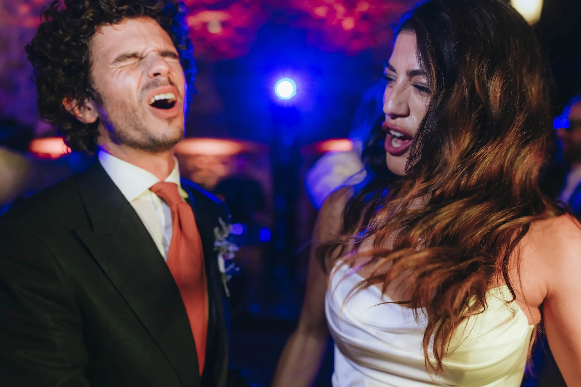 A man and woman are dancing and singing at a party or celebration with colorful lighting.