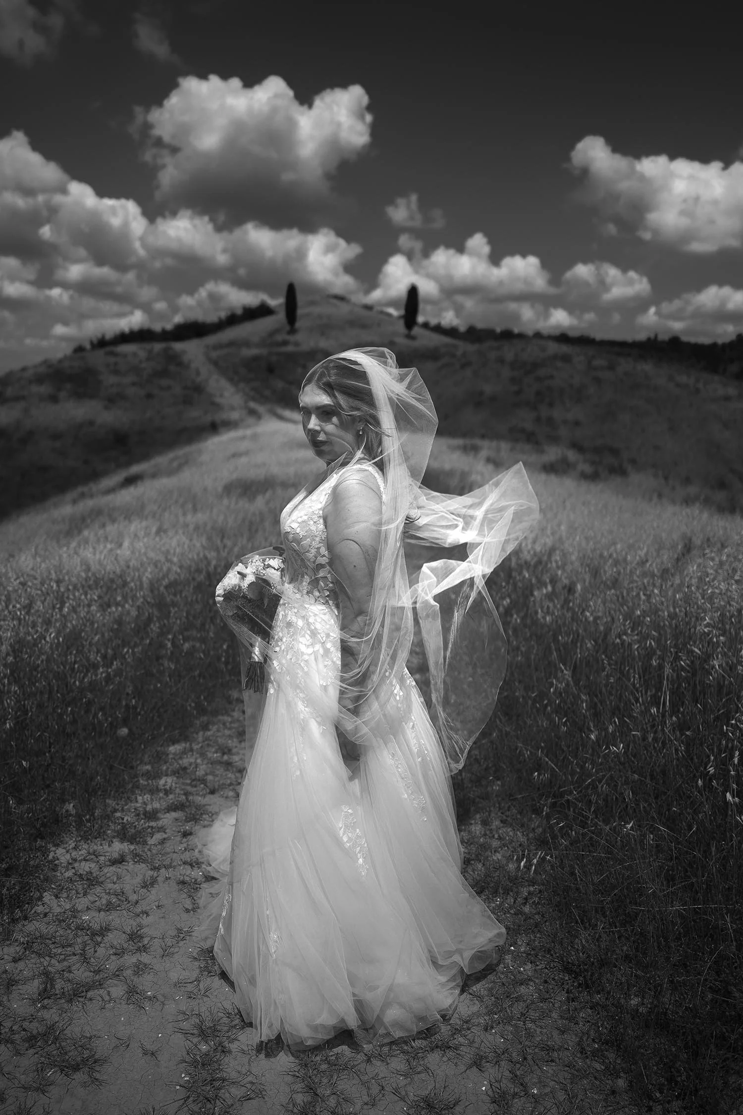 timeless and artistic portrait of the bride covered with the veil blowing in the wind on a typical tuscany hill with cypresses on top near Quercia al Poggio
