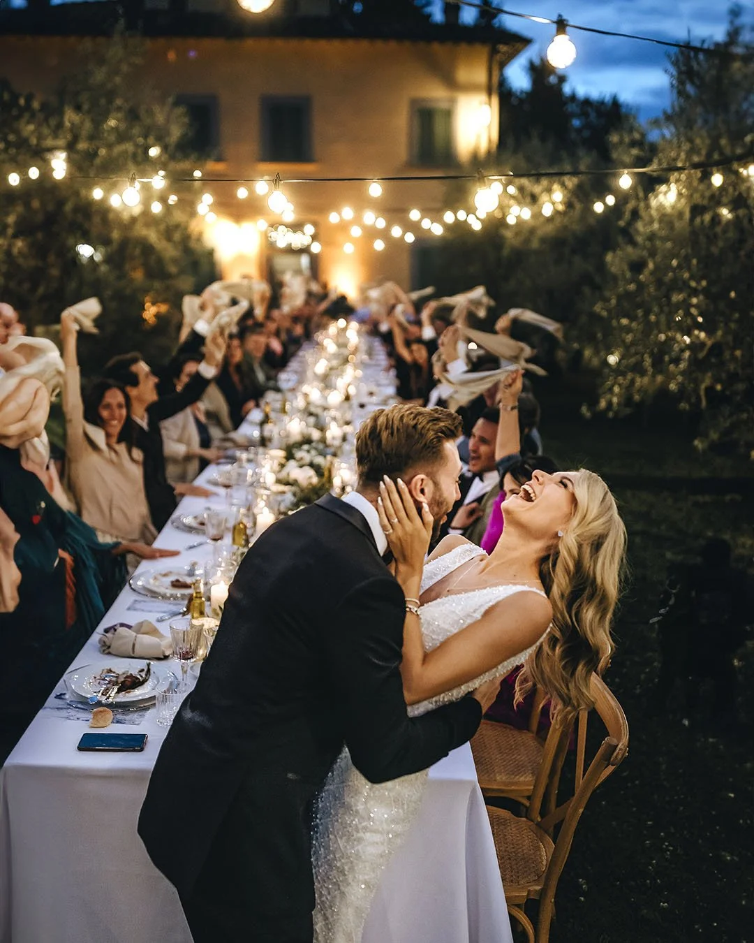 Bride and groom kiss each other with the guests sitting at the table