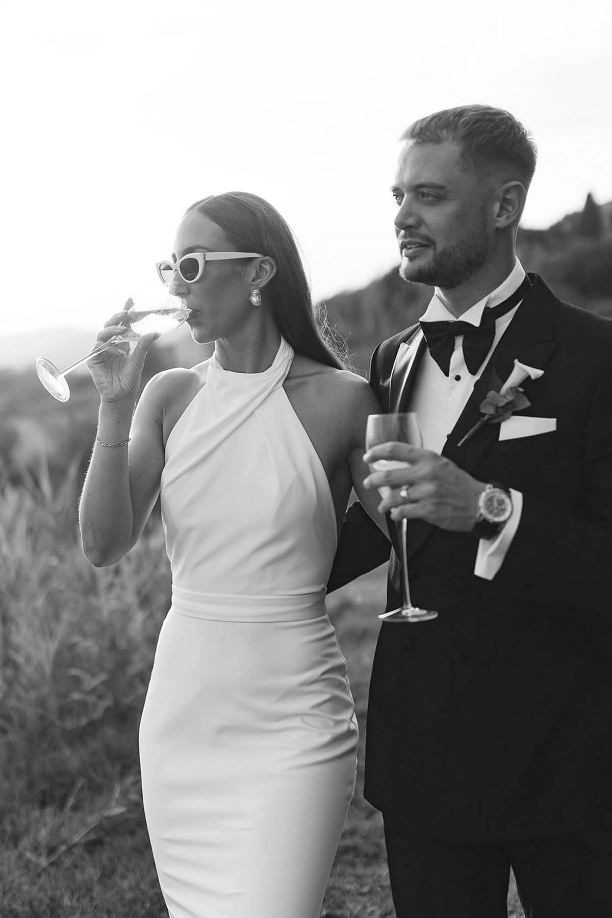 bride and groom with sunglasses holding drink and walking together