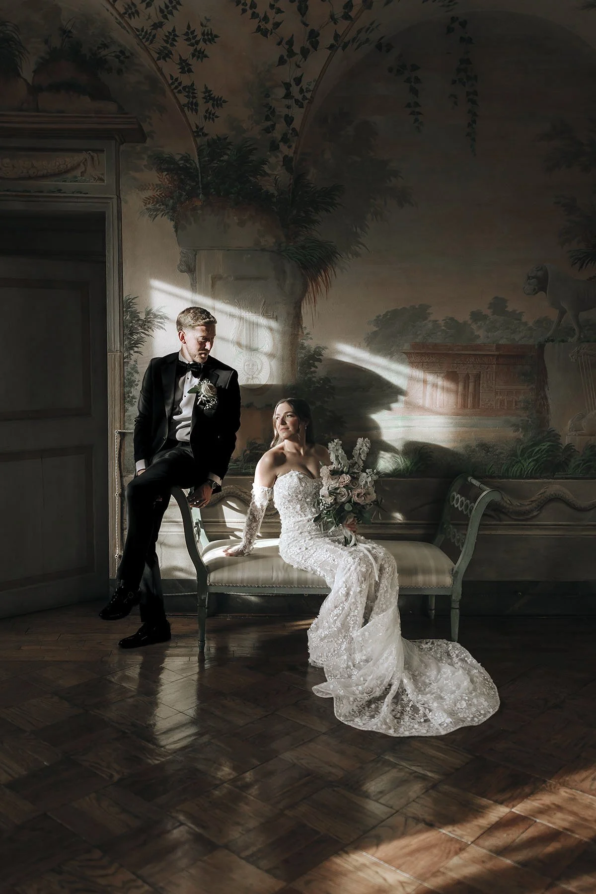 Iconic portrait of bride and groom sitting on a sofa in a stunning room at Villa di Catignano in Tuscany. The dramatic light and shadows creates a timeless and magazine oriented portrait. Photo by Rellini art studio, best wedding photographers in Umb