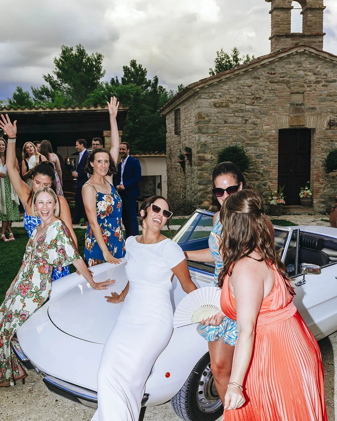 Bride celebrating with her bridesmaids sitting on a vintage convertible car