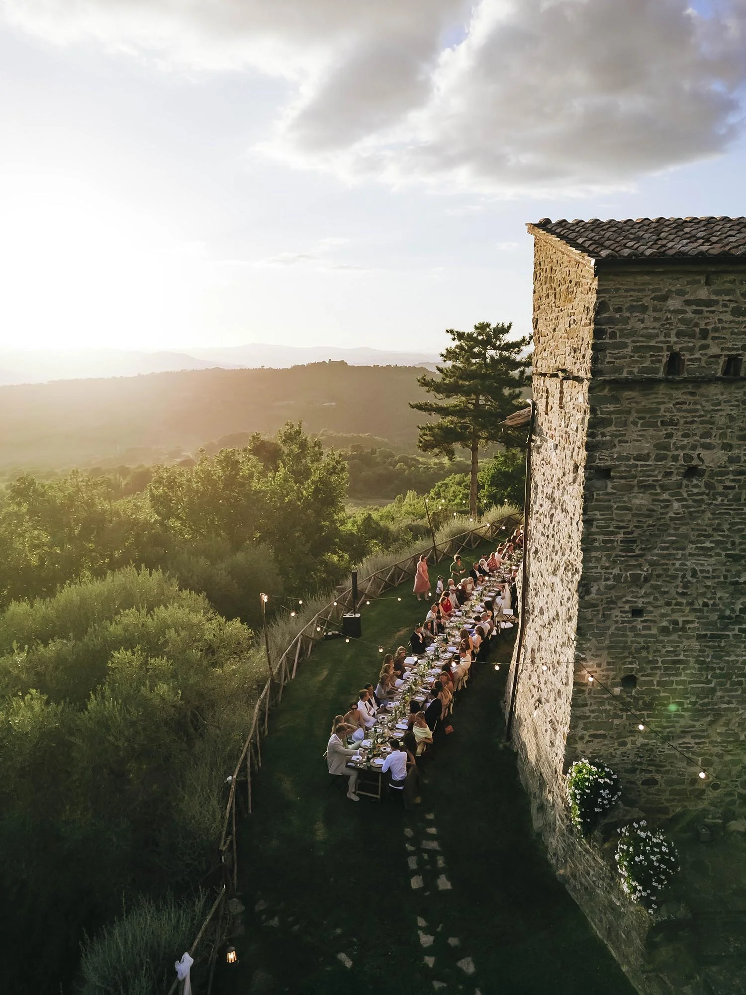 Aerial view of a wedding dinner by a castle at sunset. photo by Rellini art studio