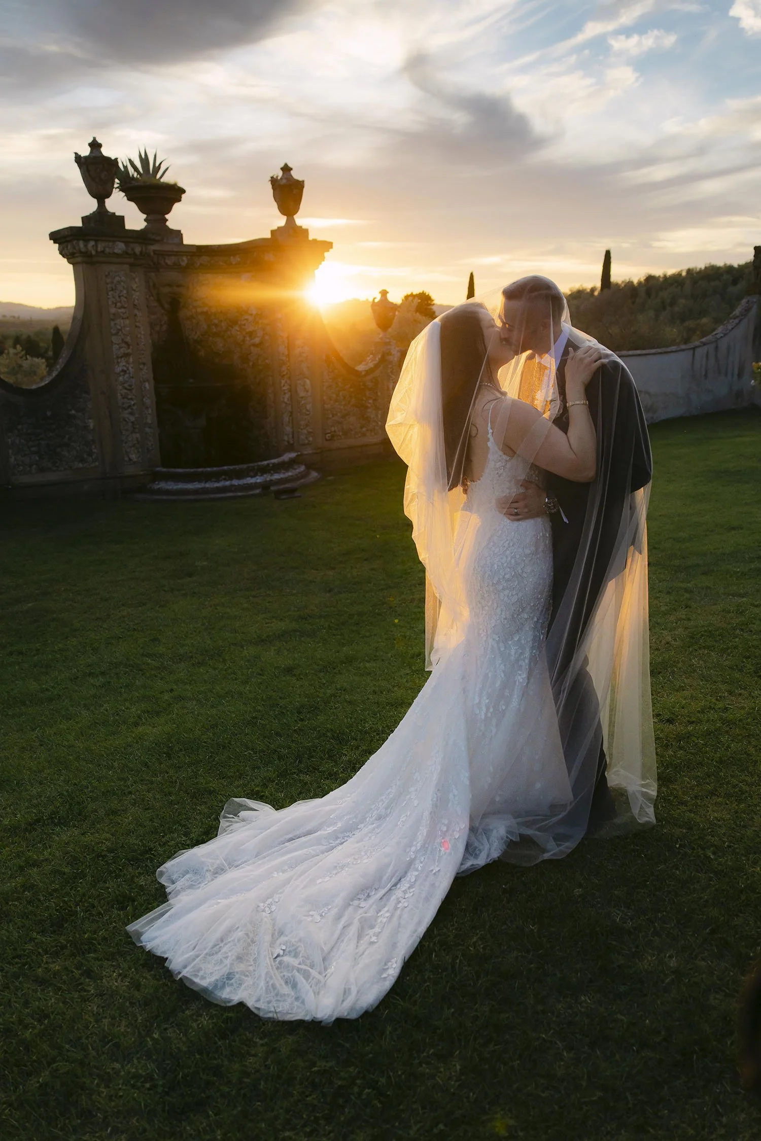 Photo of bride and groom kissing under the veil lit by a warm sunset light