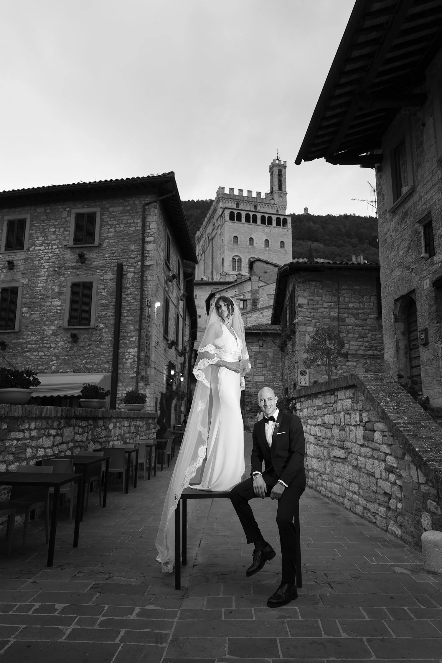 bride and groom posing along a road in Gubbio. the bride is standing on a table