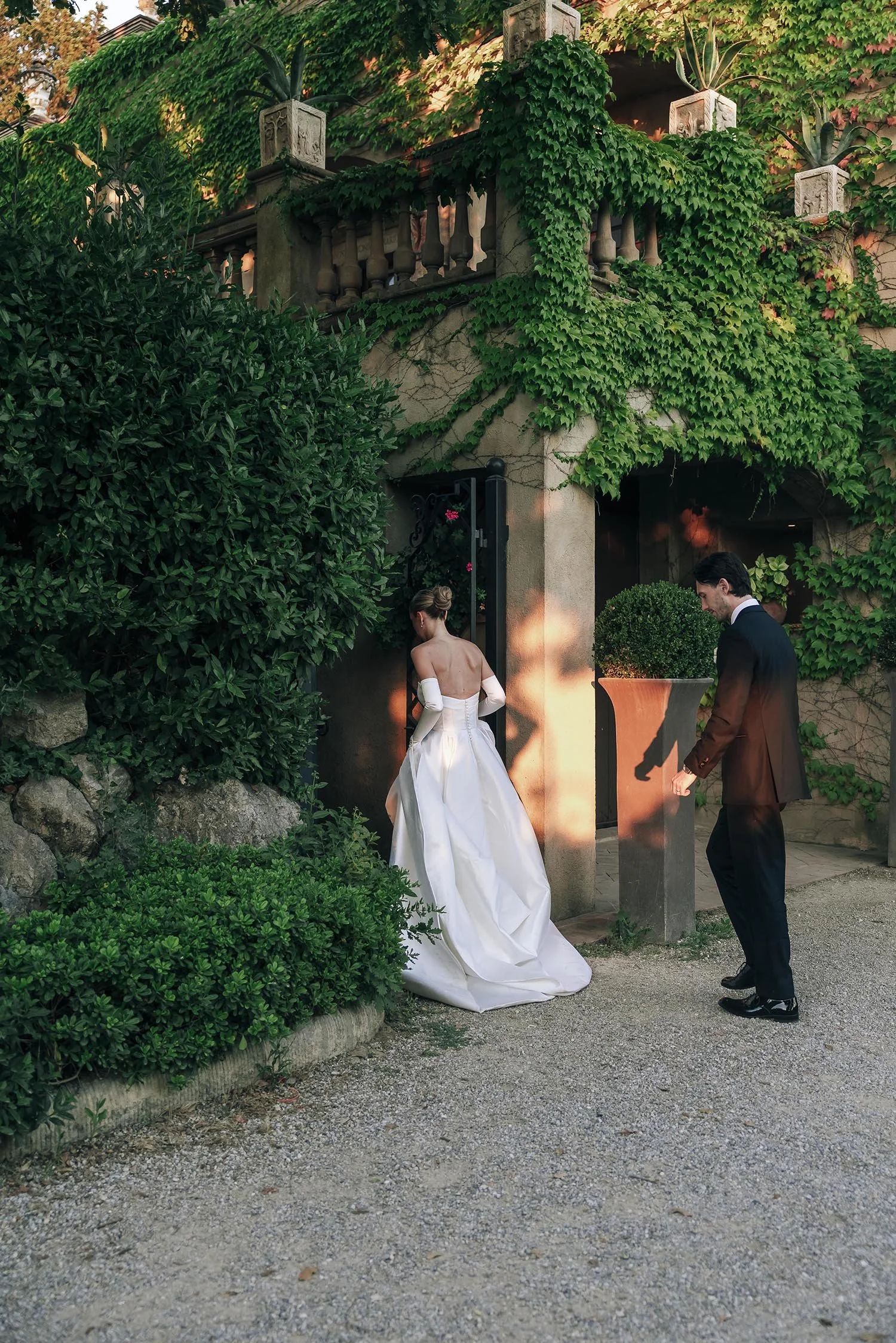 Bride and groom walking together in the doorway between the cypresses at sunset
