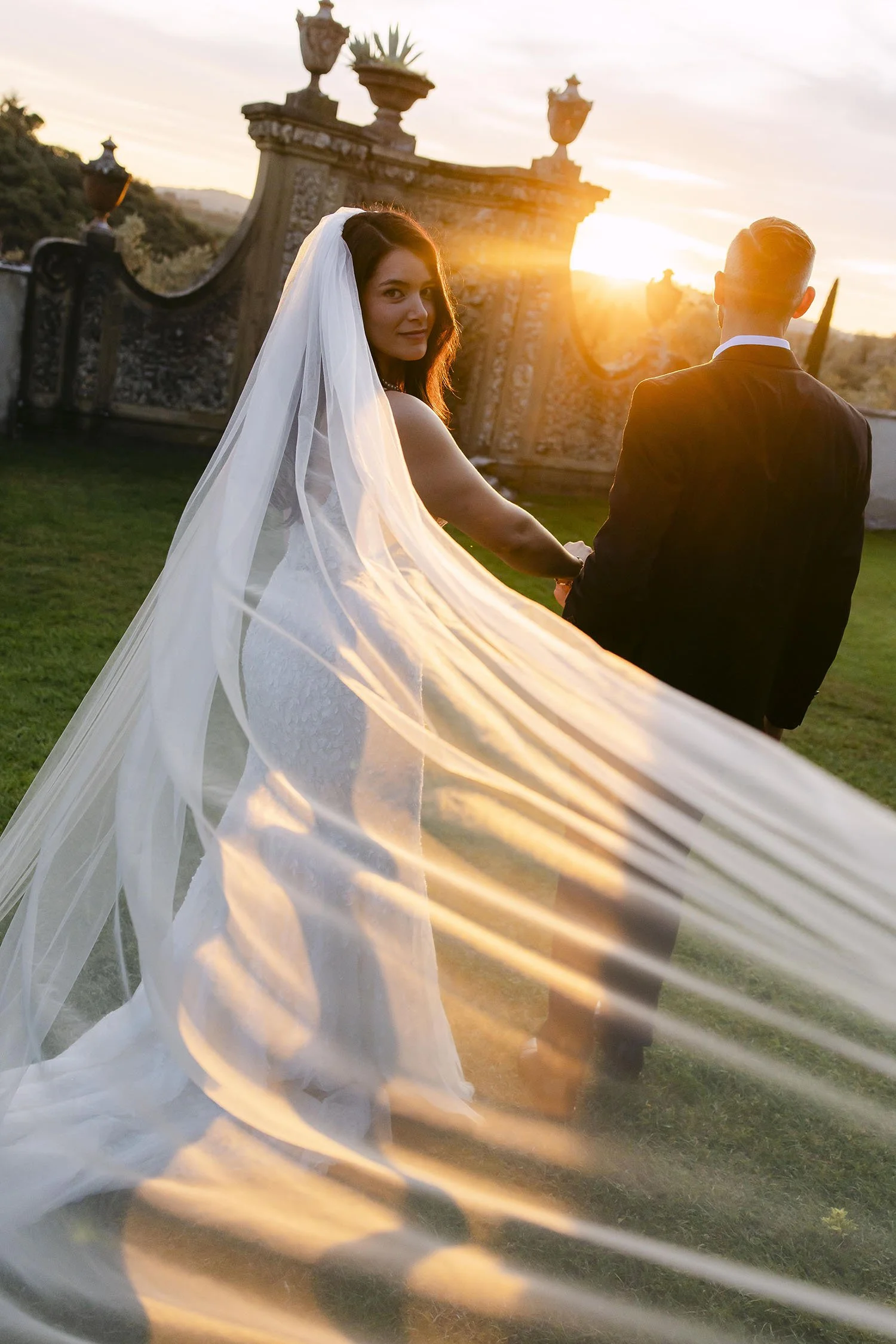 Bride and groom walking together with a warm sunset light and the bride is half covered by the veil with the iconic architecture of Villa Medicea di Lilliano