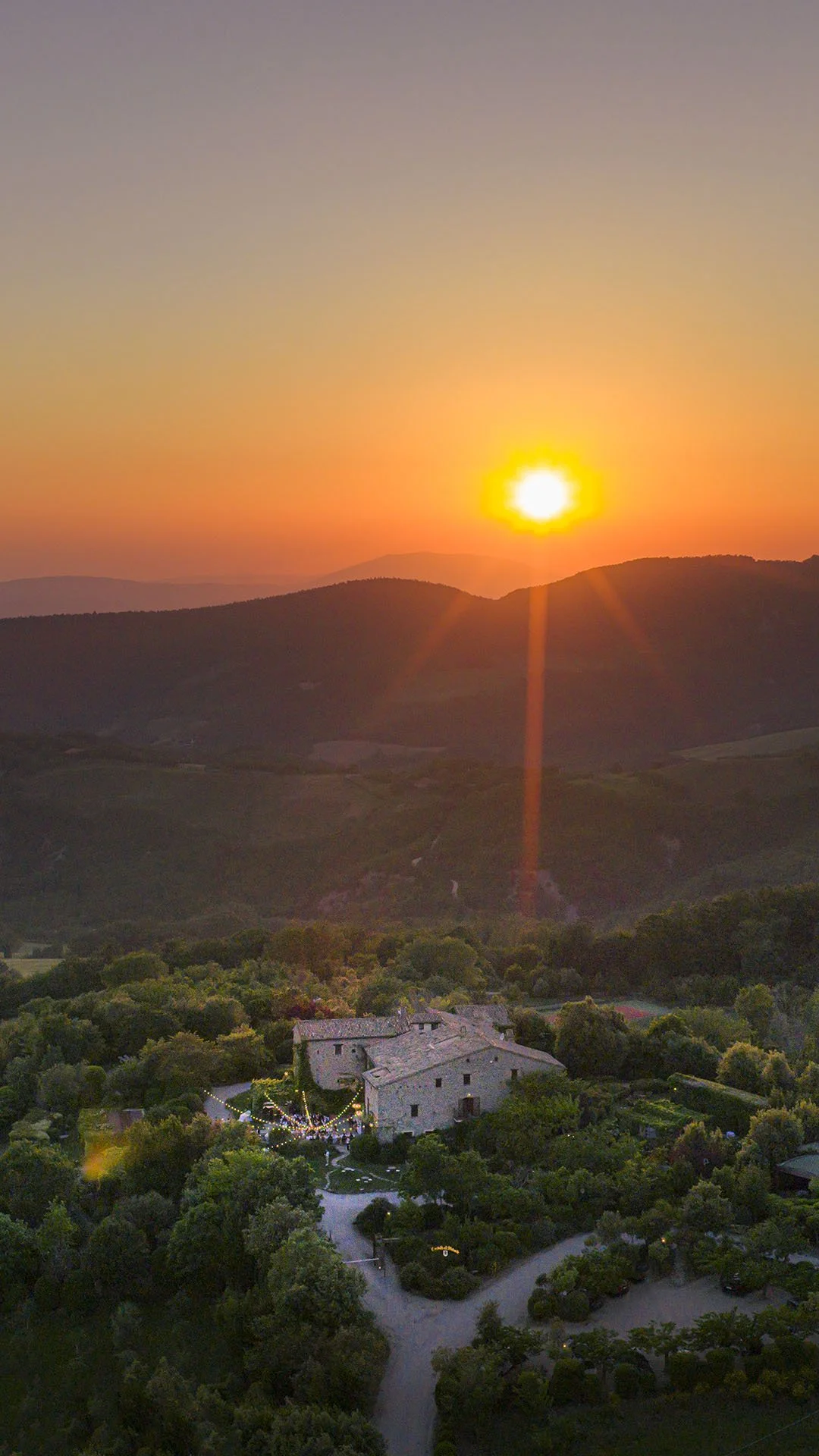 aerial view of Castello di Petrata at sunset with the guests having dinner al fresco under the fairy lights