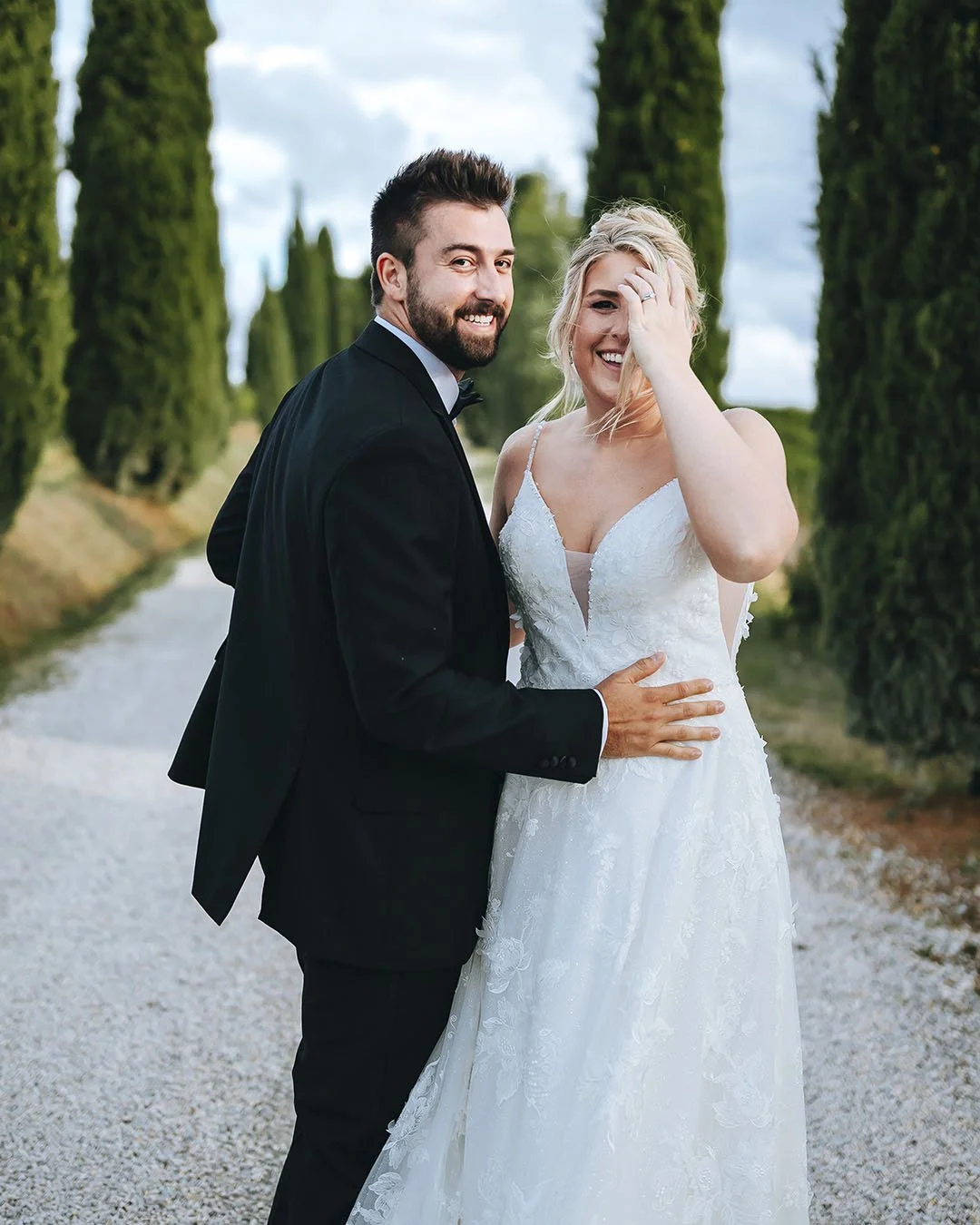 Bride and groom playing with each other along a road with cypresses
