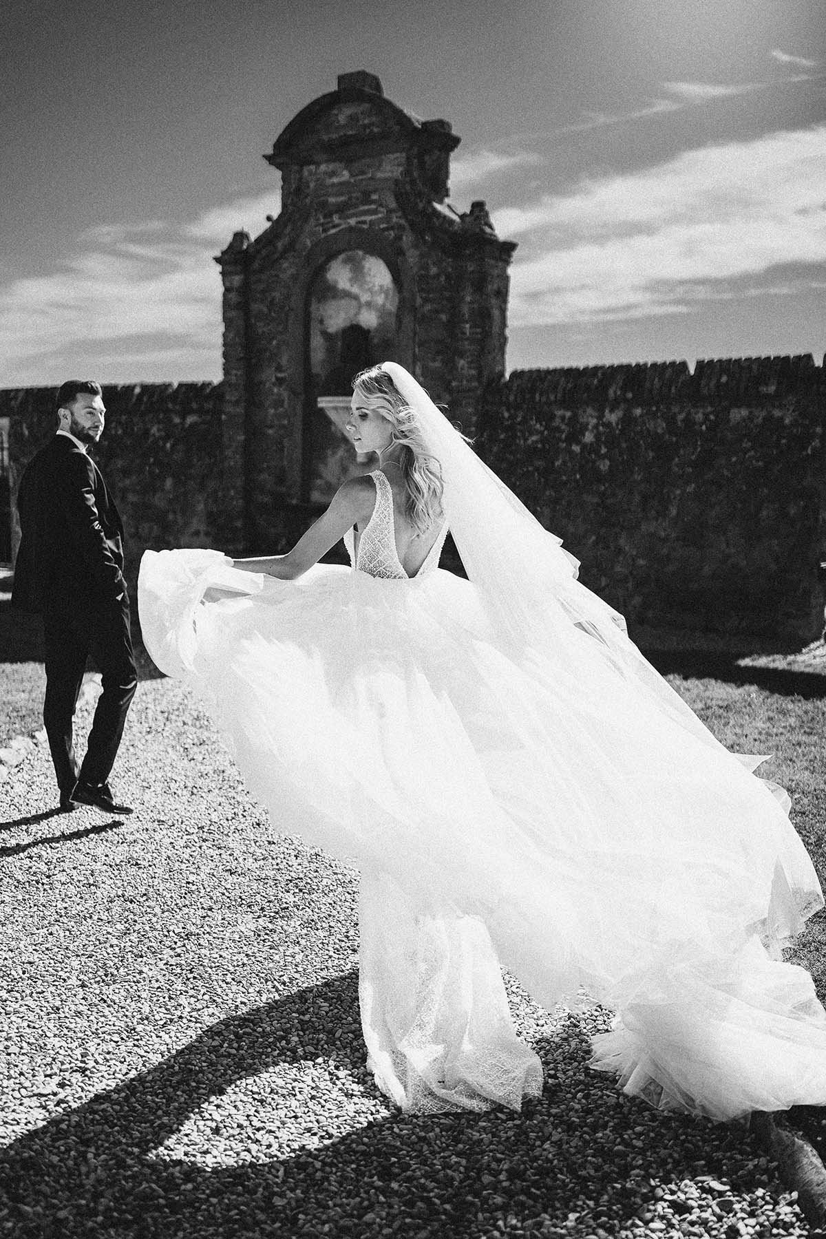 Artistic photo of bride and groom walking together after their ceremony in Tuscany. The bride holds the dress and looks elegant and gorgeous. Photo by Rellini art studio best wedding photographer in Umbria