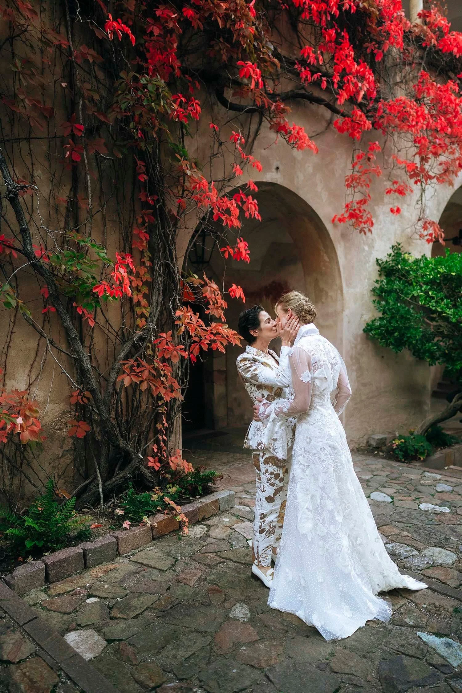 Romantic kiss under the autumn red leaves of two brides at Schloss Freudenstein in Bolzano, same sex wedding photographer in Italy.