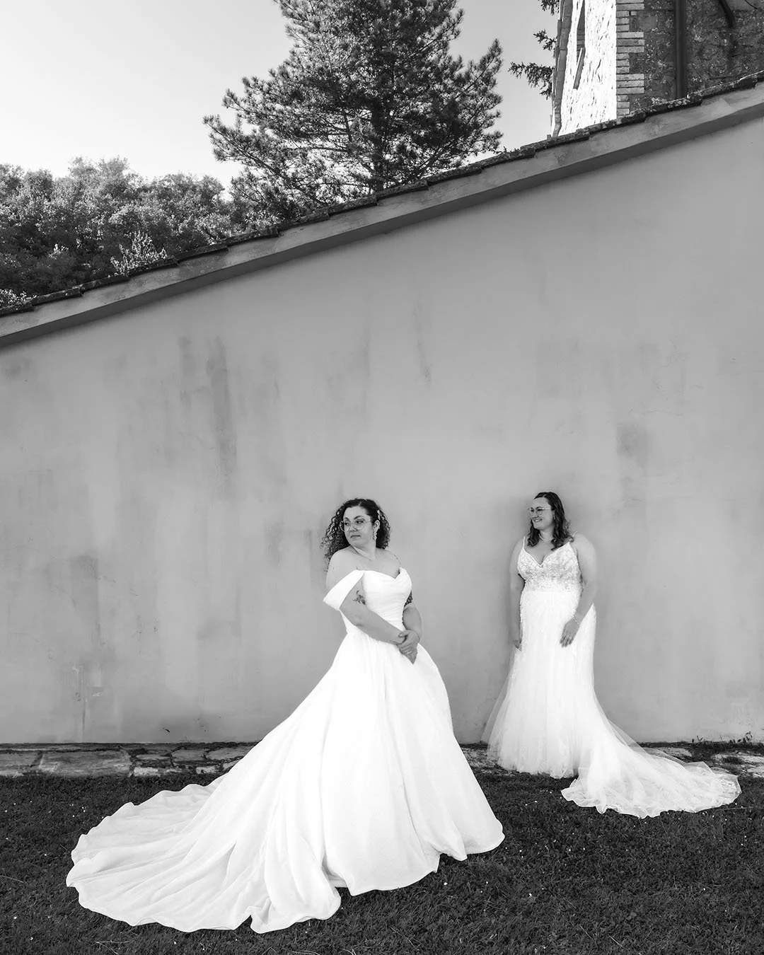 Two brides posing in their white dresses against a wall
