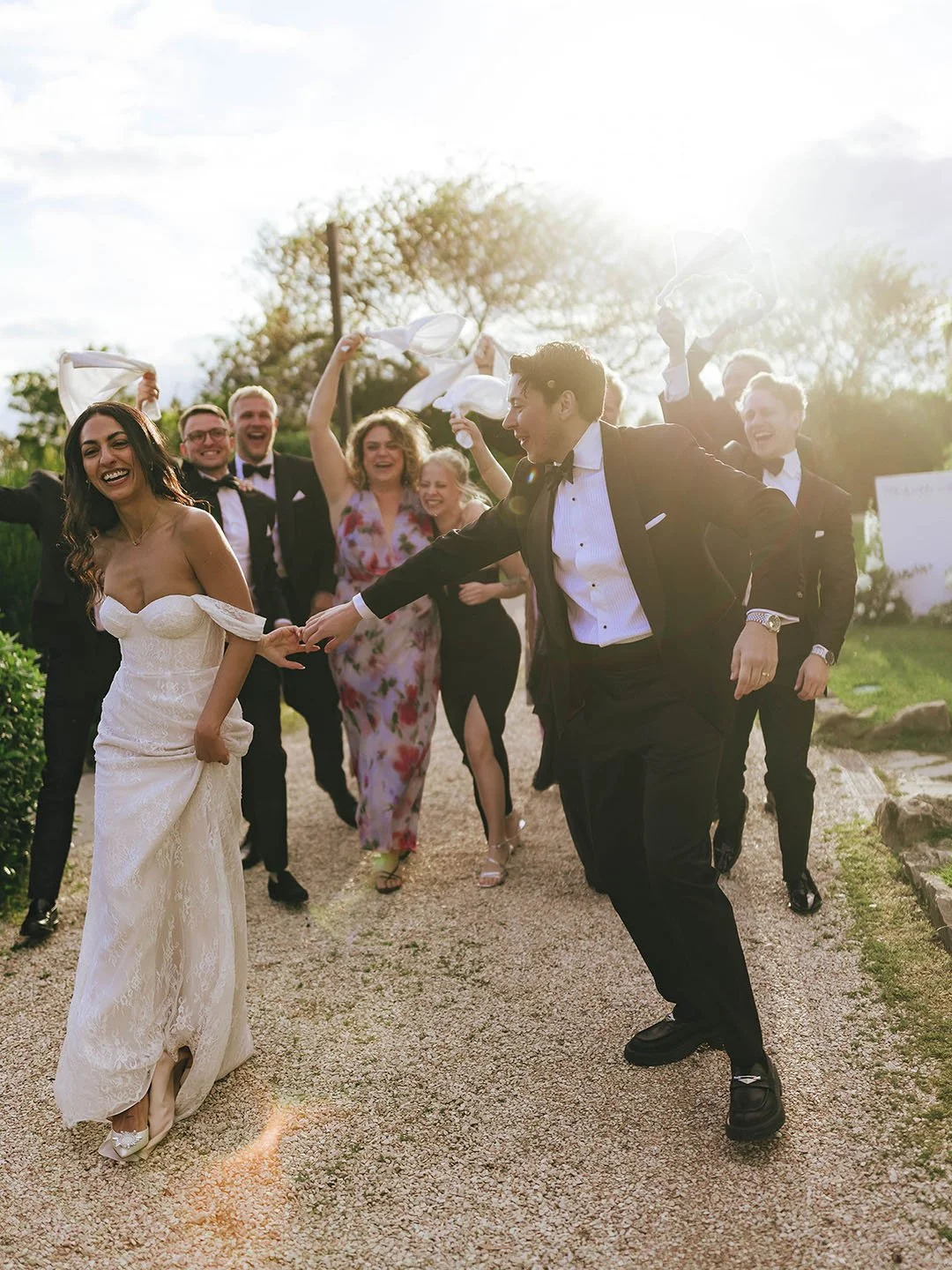 Bride and groom walking together and having fun dancing followed by their bridal party and friends at sunset