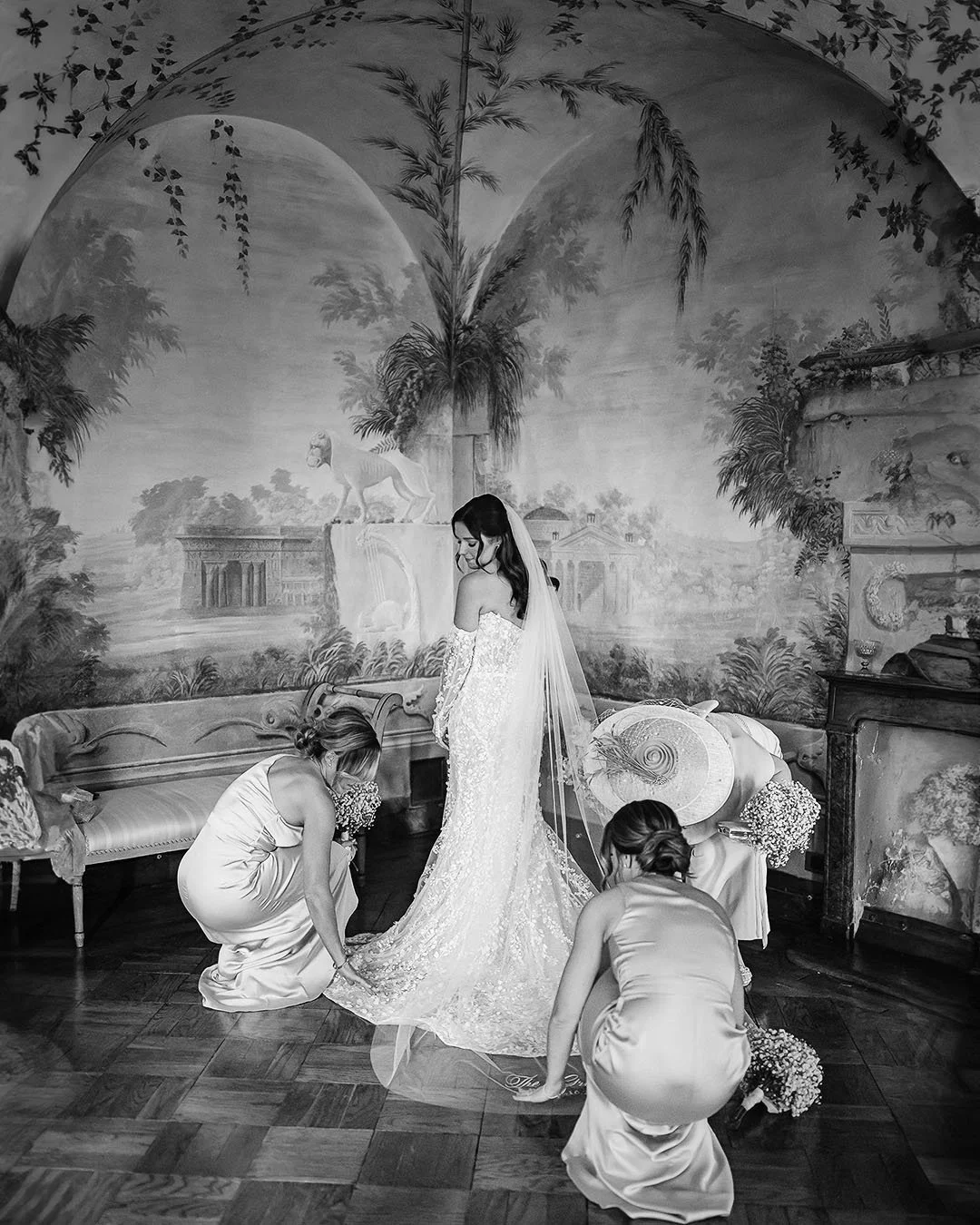 Bridesmaids helping fixing the dress of the bride in a room with frescoes
