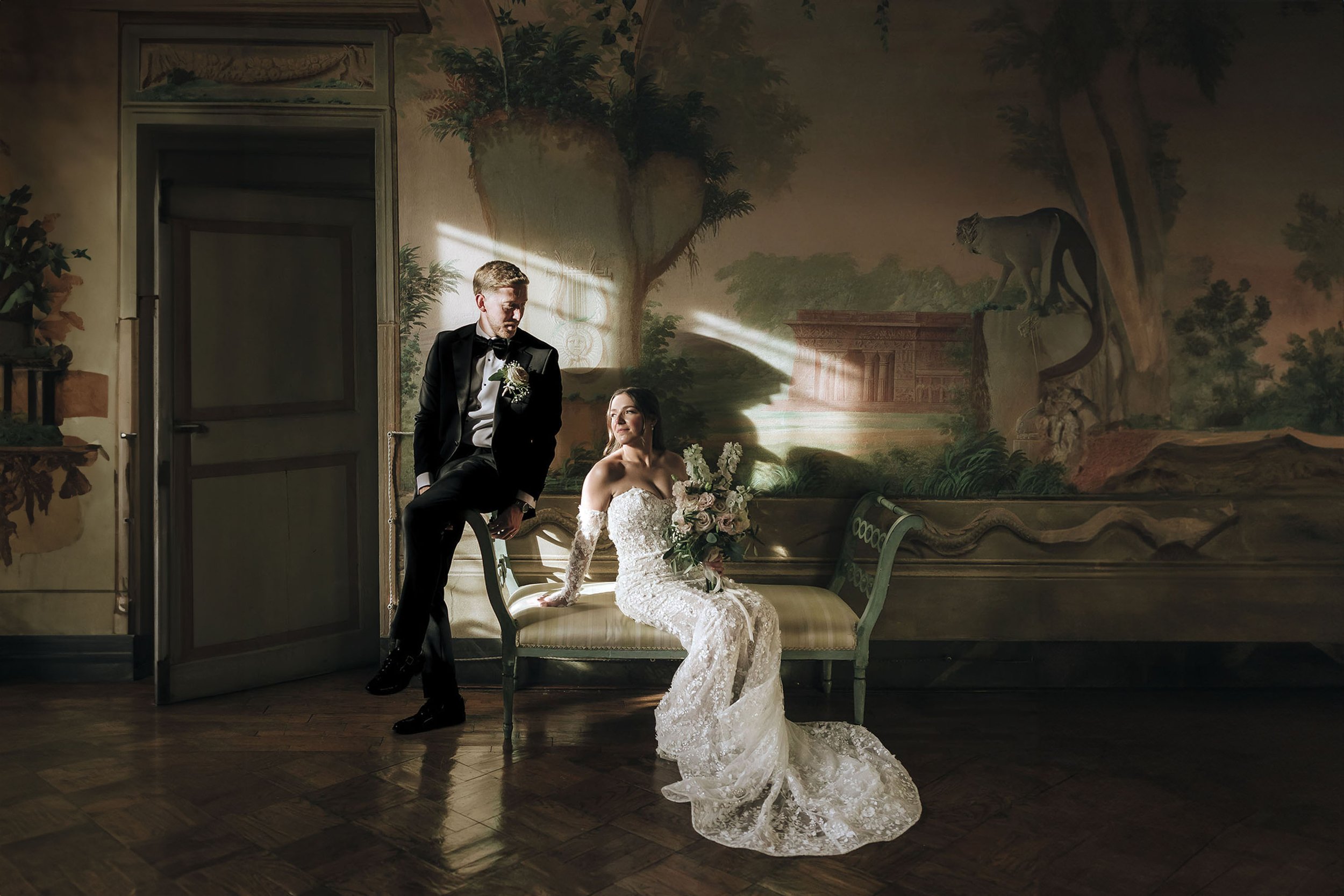 bride and groom sitting on the sofa in a room with frescoes with a dramatic light