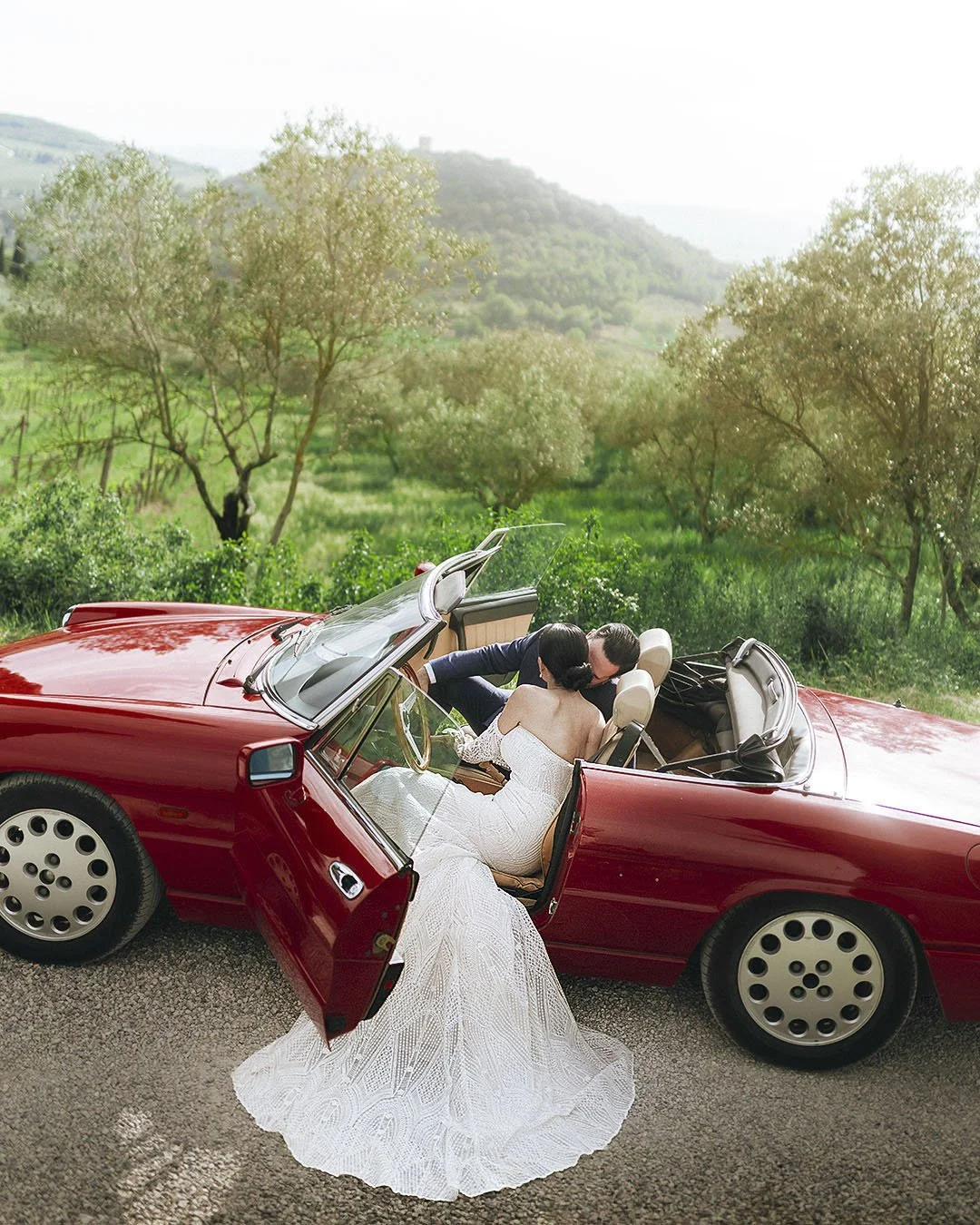 bride and groom kiss in a red vintage car  at Terre di Nano wedding venue in Siena. Photo by Rellini art studio best wedding photographer in Siena