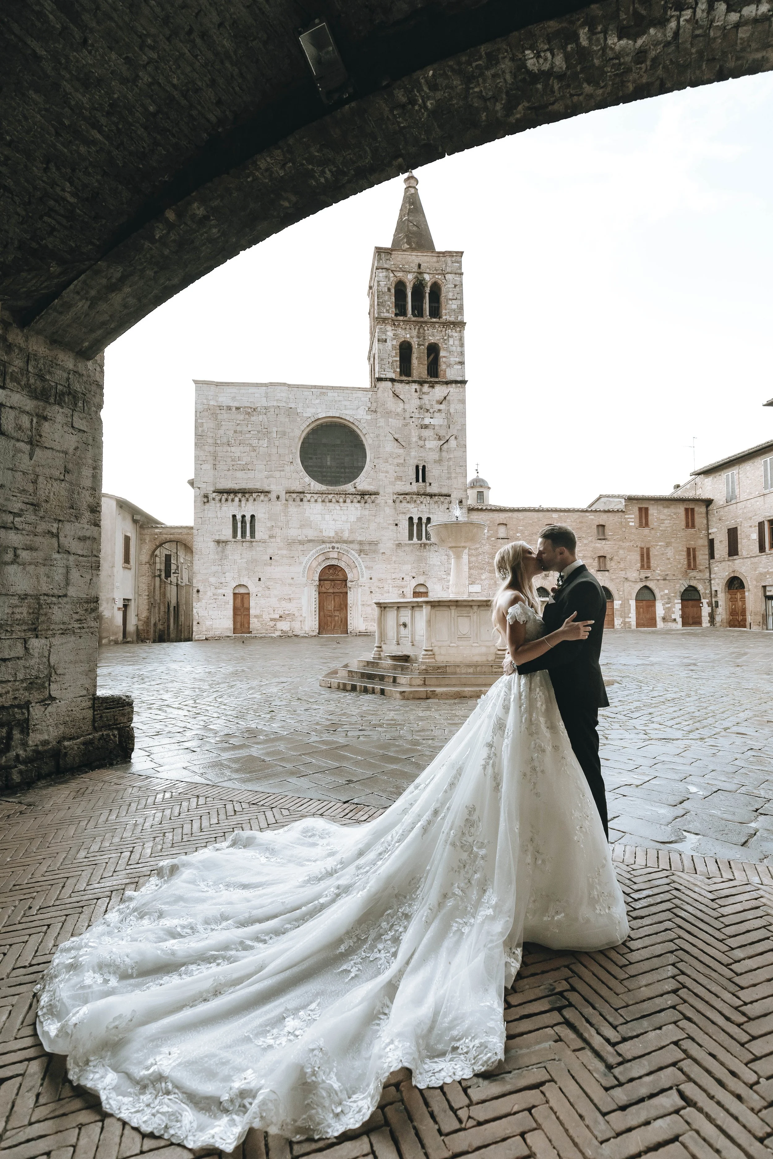 bride and groom kiss each other in an empty square in Umbria