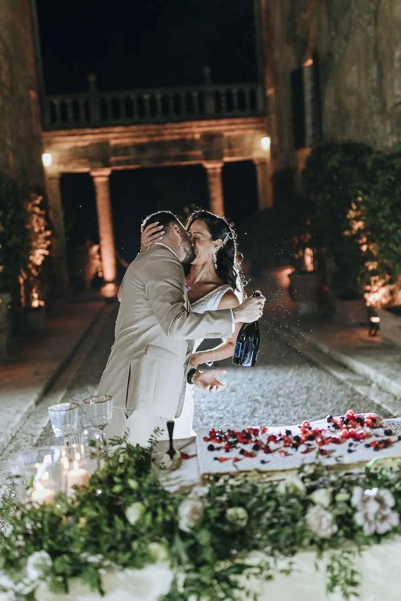 Bride and groom kissing each other while cutting the cake by night at Borgo Stomennano. Photo by Rellini art studio best wedding photographer in Umbria