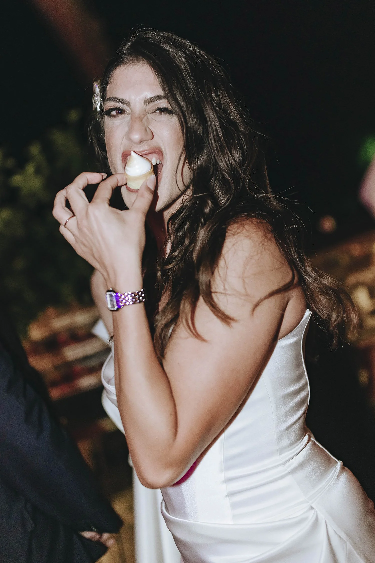 Woman in white satin dress having fun at a celebration, eating cake or dessert.