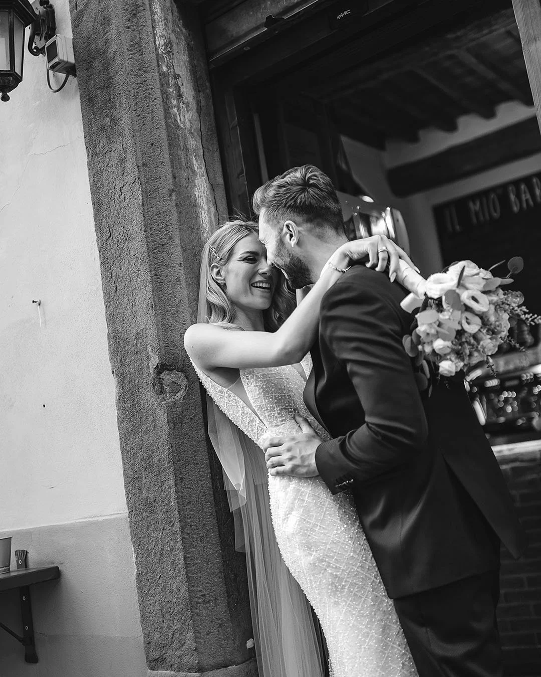 Bride and groom holding each together leaning against the door of a bar
