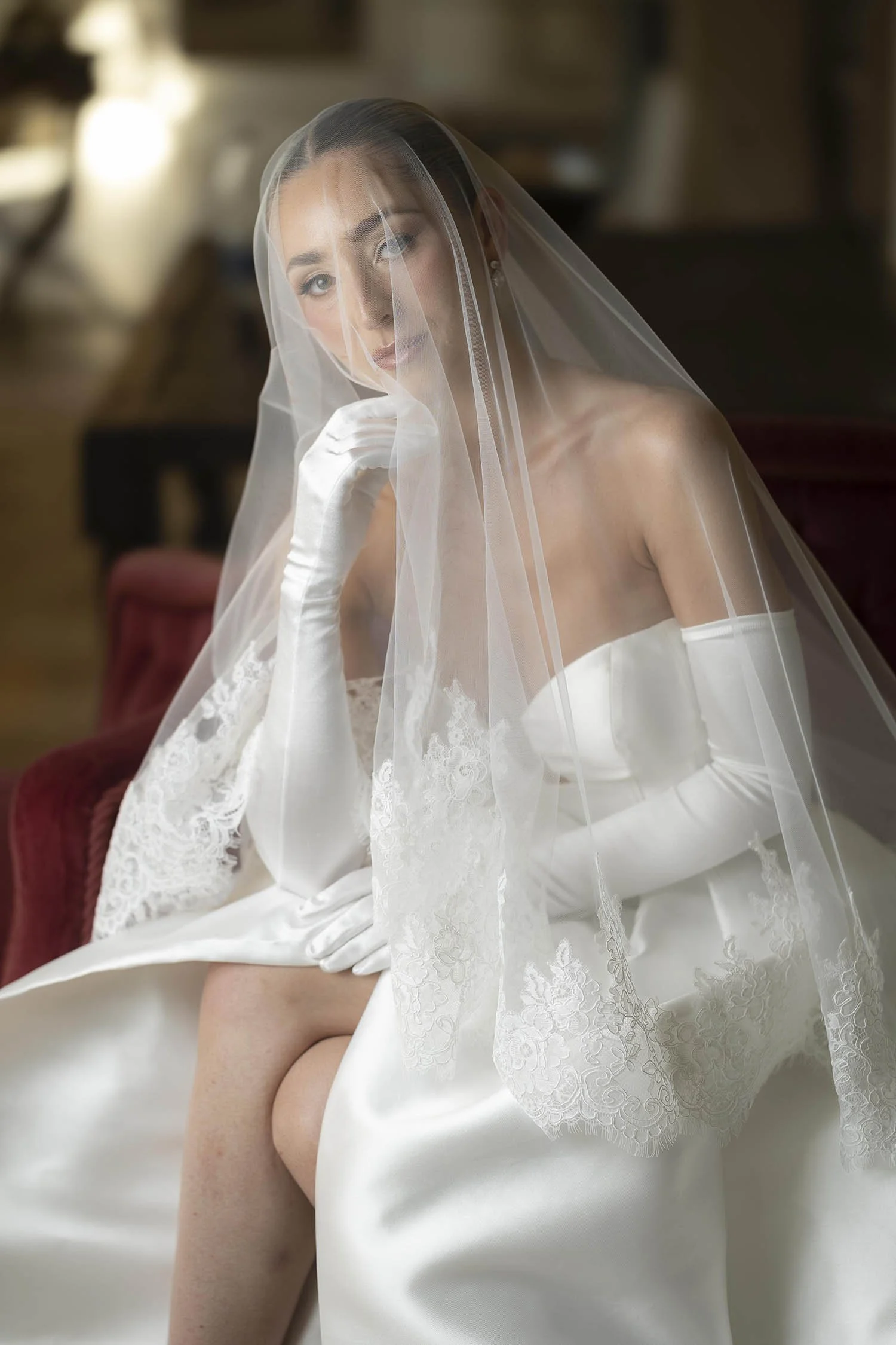 the bride sitting on a sofa and posing under te veil