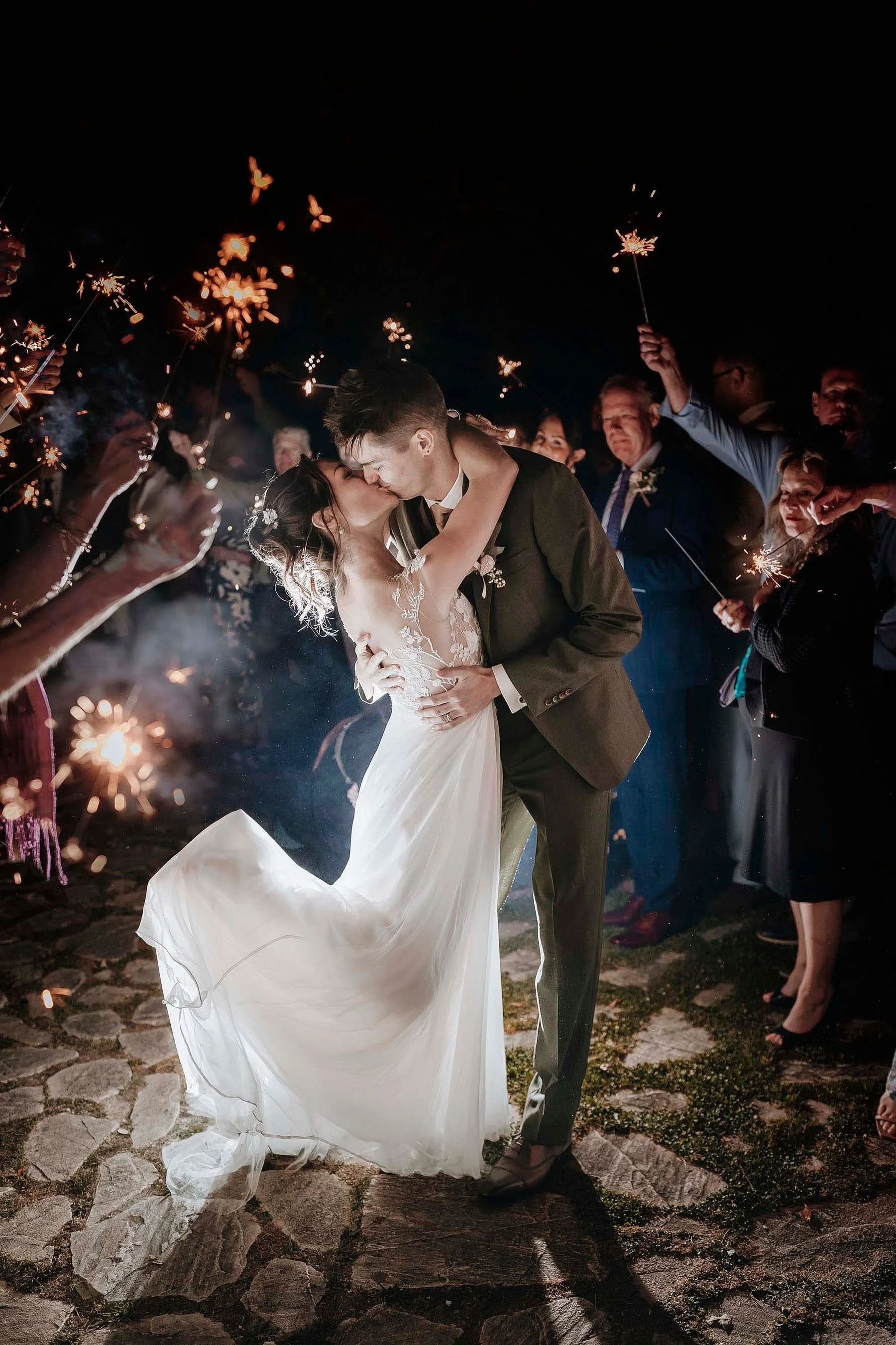 Bride and groom kissing each other lit by the sparklers held by their guests, Wedding party at Castello di Petrata in Umbria