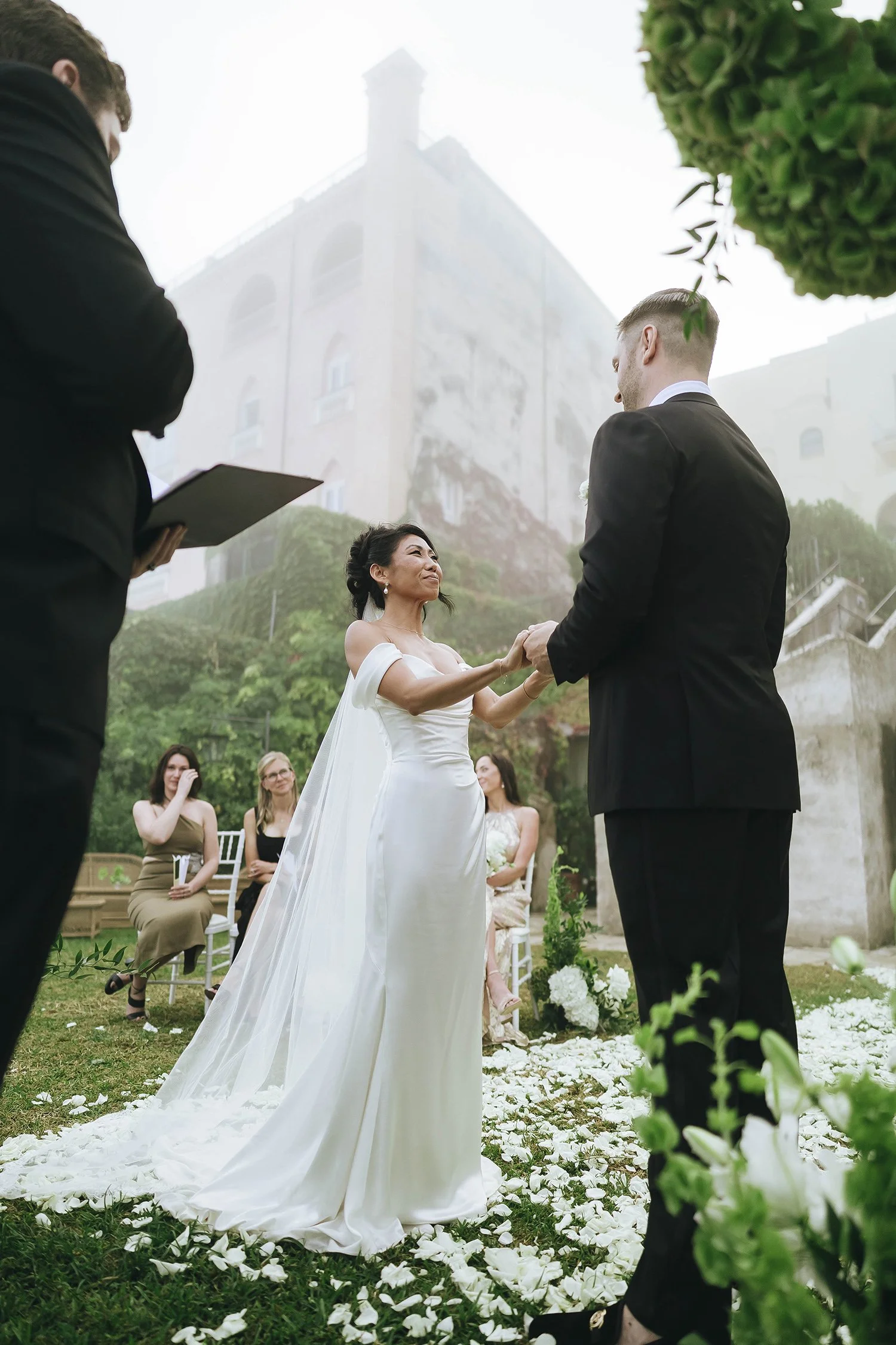 Timeless and fashion magazine style photo of bride and groom looking elegant and exchanging vows during their ceremony at Belmond Hotel Caruso in Ravello for their destination wedding in Ravello. Photo by Rellini art studio wedding photographer