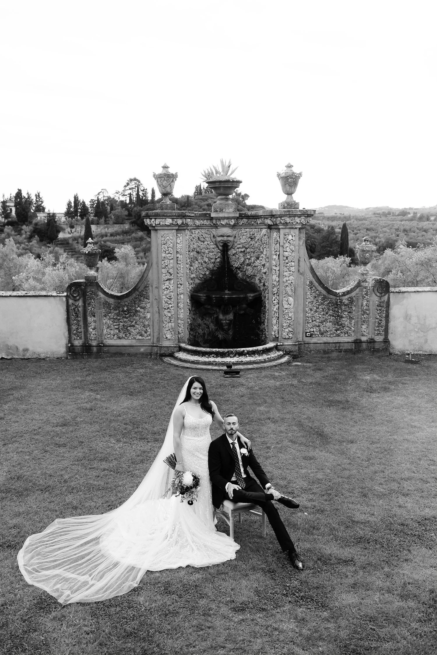 Portrait of the groom seated and the bride standing behind him with the iconic architecture of VIlla Medicea di Lilliano in the background