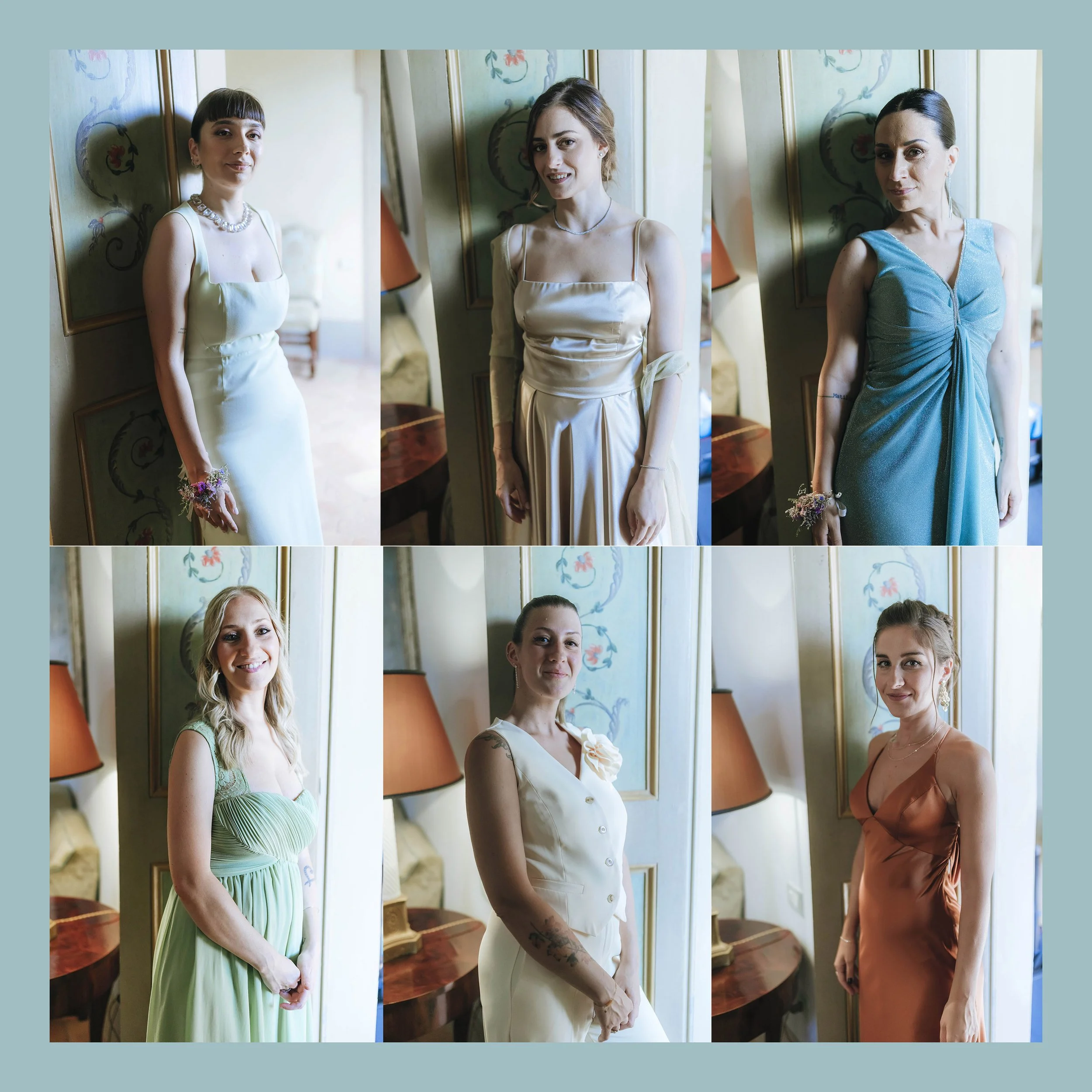 Six women dressed in elegant dresses posing indoors with floral artwork and table lamps in the background.