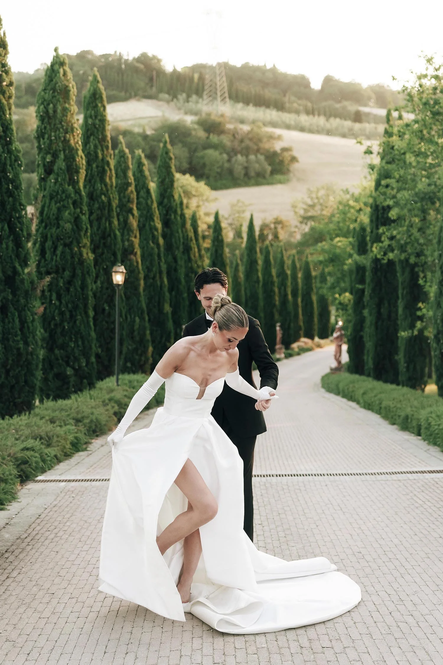 Bride and groom walking together in the doorway between the cypresses at sunset