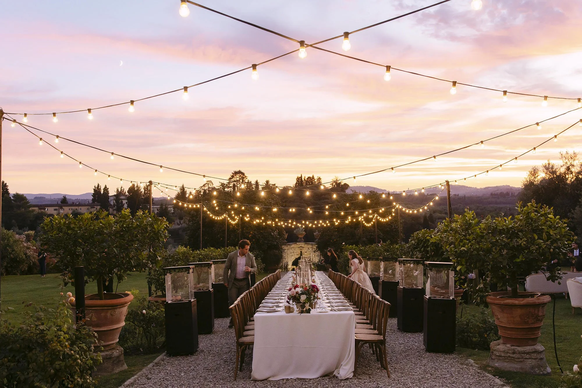 The dinner table under the fairy lights with a colorful sky at sunset