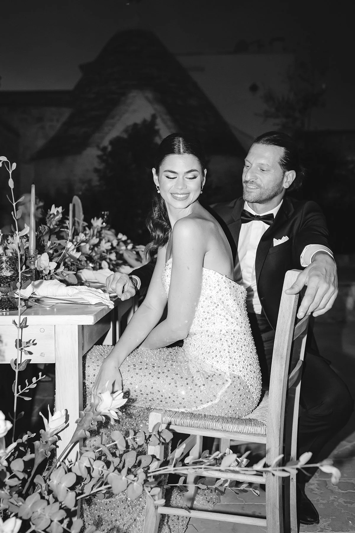 bride and groom sitting next to each other and looking at each other during a dinner reception