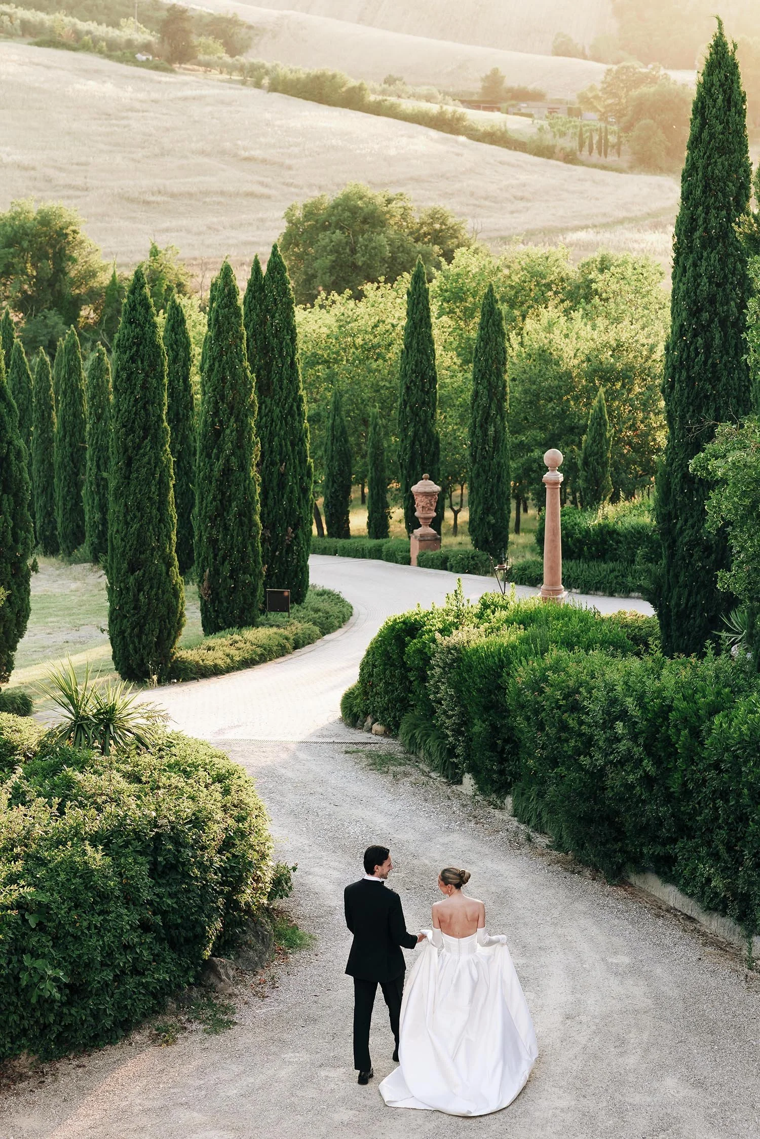 bride and groom walk together at Tenuta Corbinaia with cypresses in the background