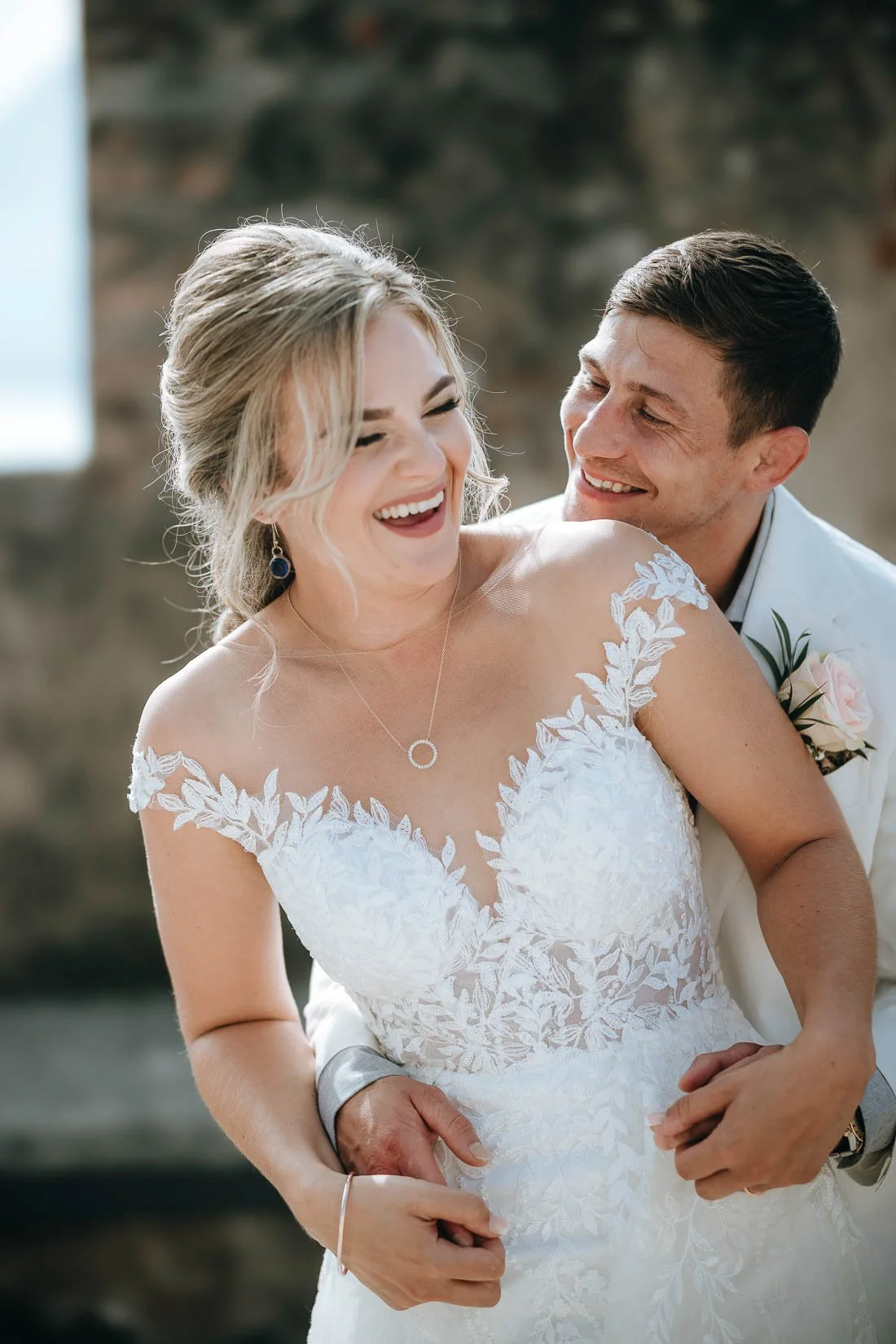 A woman in a wedding dress and a man in a suit celebrating. They are smiling and laughing, embracing each other, with a blurred background.