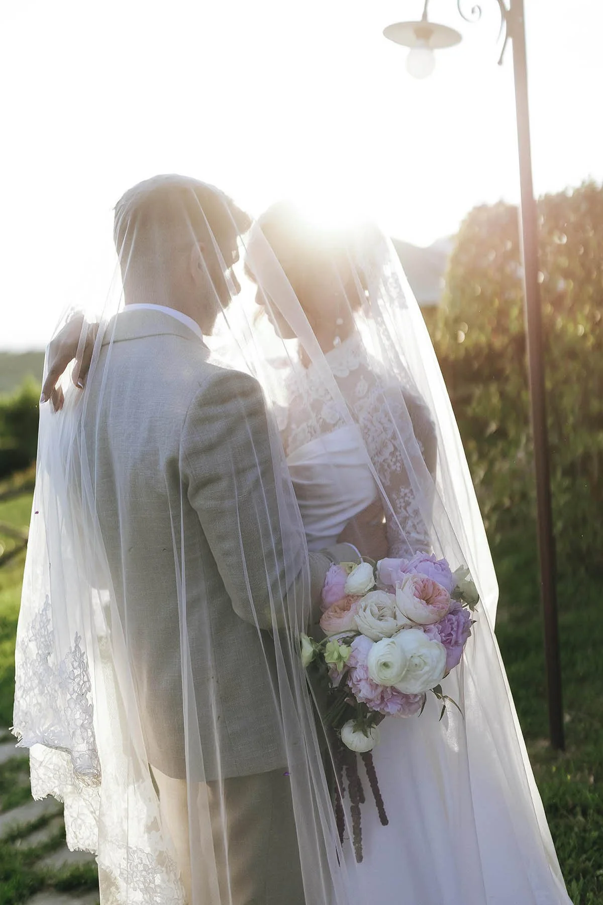 Bride and groom holding each other under the veil at sunset