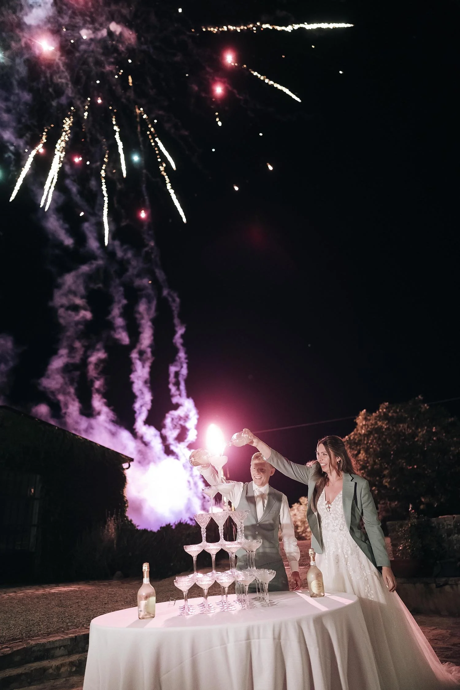 bride and groom with a champagne tower and fireworks in the background