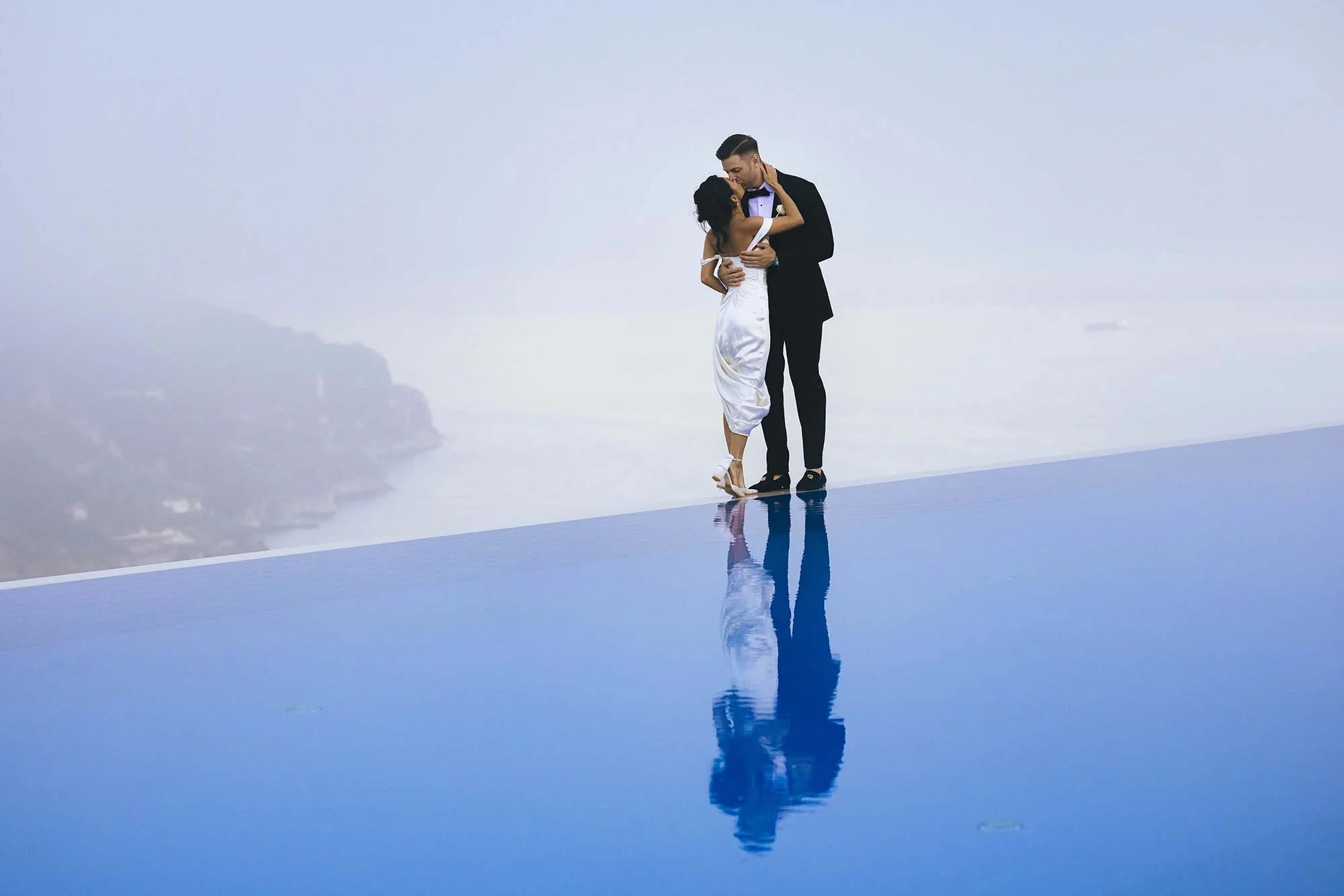 Iconic photo of bride and groom kissing on the edge of the infinity pool with the Amalfi coast in the background. Photo by Rellini art studio
