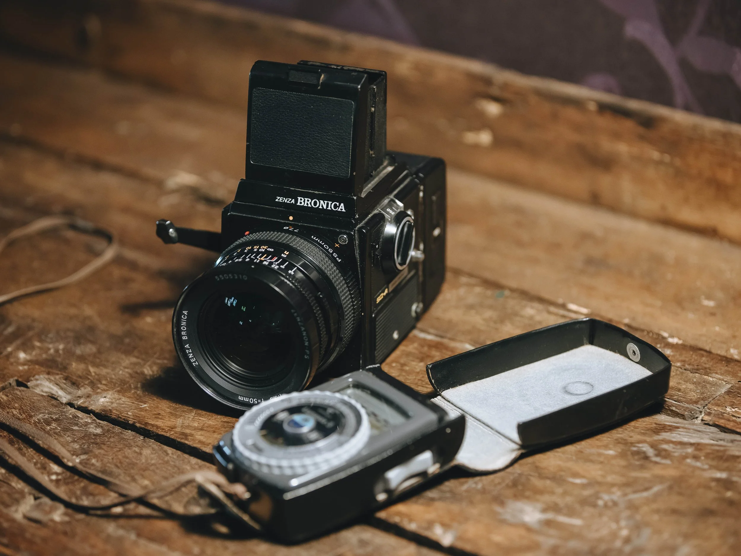 A vintage Zenza Bronica camera with a lens and a separate flash, placed on a rustic wooden surface. Analogue film photographers in Italy