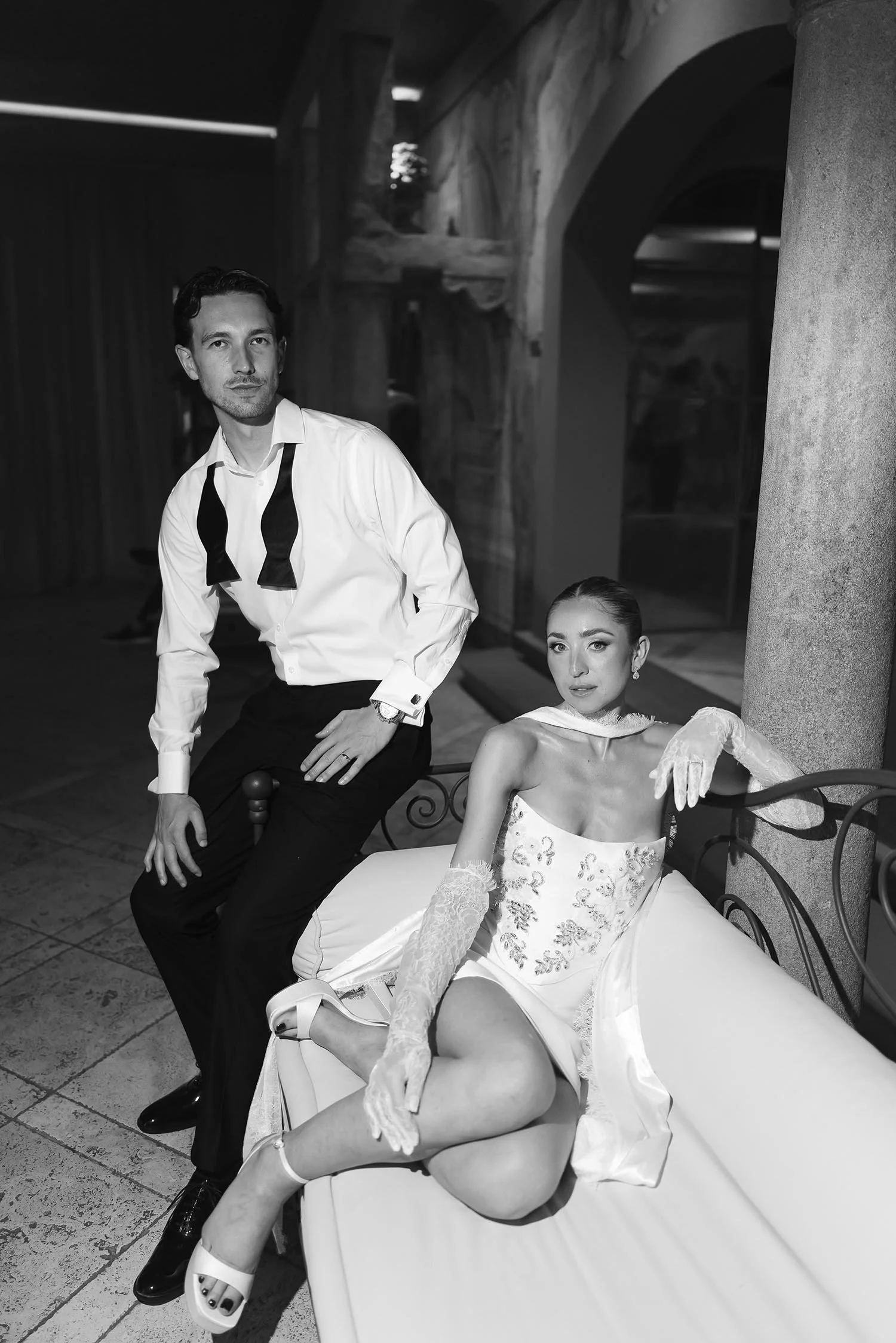 Bride sitting on a sofa with the groom looking elegant in their party dresses